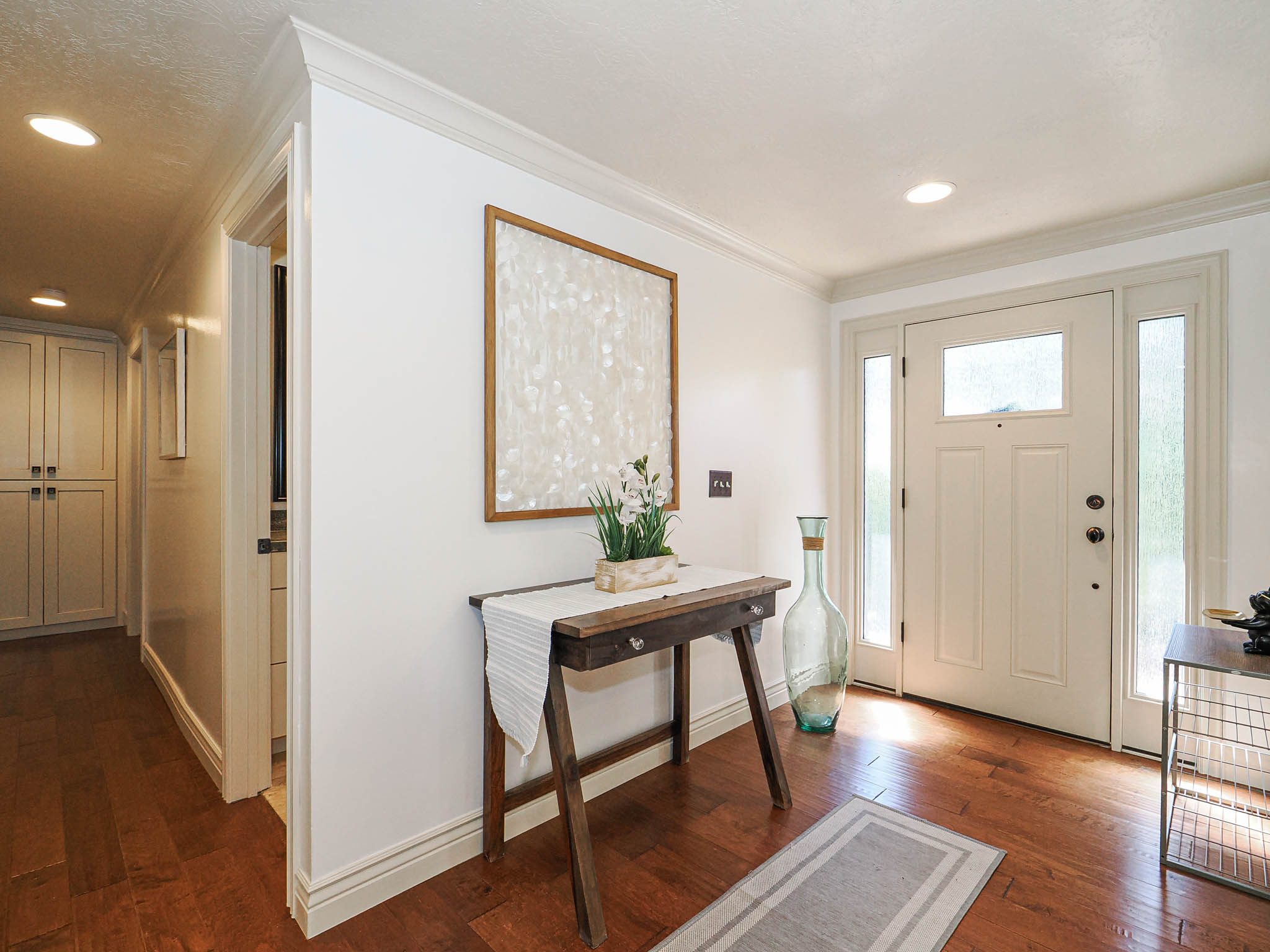 Entryway featuring a paneled door with sidelight windows, rich wood-finish flooring, recessed lighting, crown molding, and built-in cabinetry in the adjacent hallway