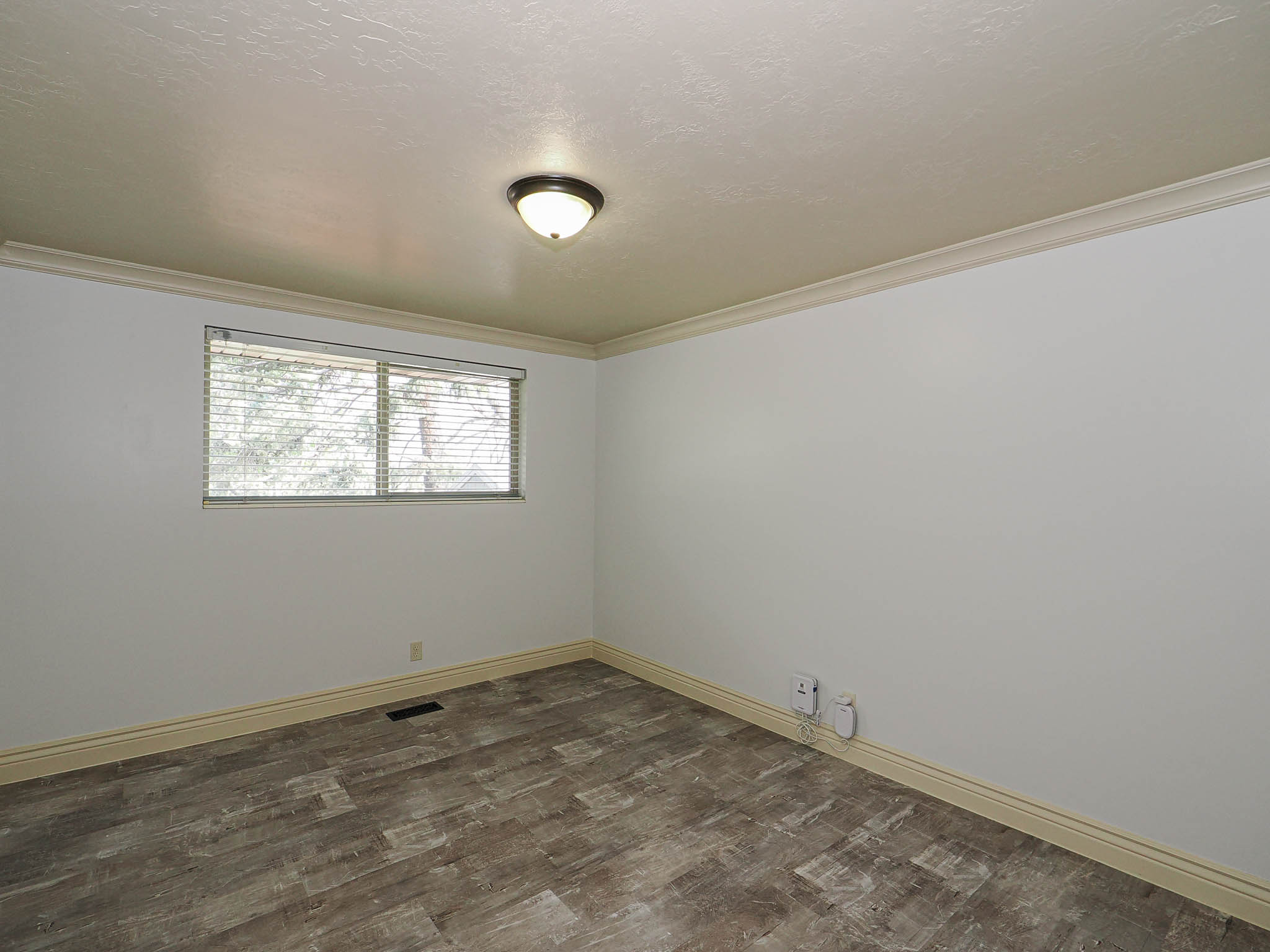 Room featuring wood-finish flooring, white walls, and a window with blinds