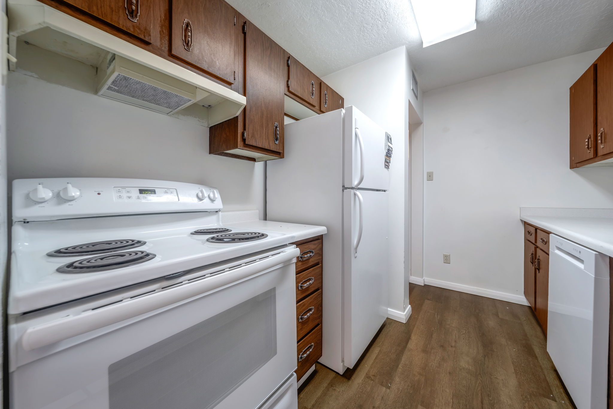 Kitchen featuring white appliances, wood-finish flooring, wood cabinetry, and white countertops