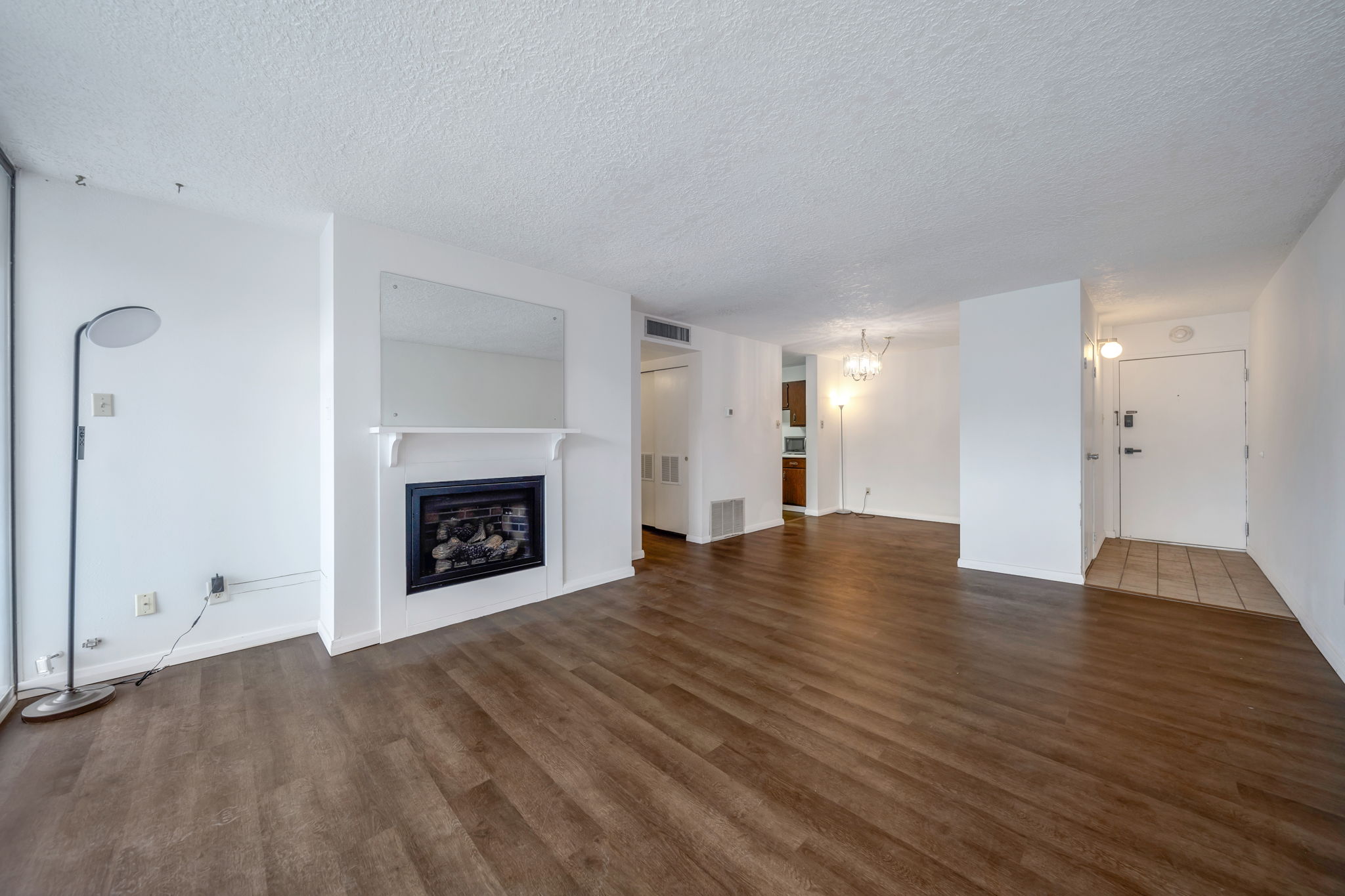 Spacious living area featuring wood-finish flooring, a fireplace with a white mantel, and a large wall-mounted mirror