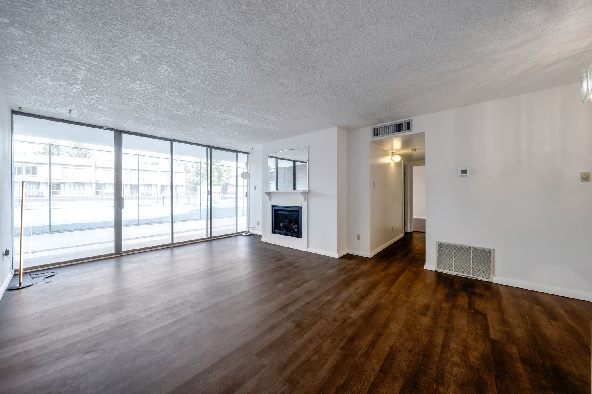 Spacious living area featuring extensive sliding glass doors, rich wood-finish flooring, a white mantel fireplace with a dark insert, a mirrored wall accent, and white painted walls