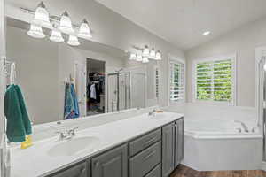 Spacious bathroom featuring a dual vanity with grey cabinetry, a large soaking tub, and a separate glass-enclosed shower