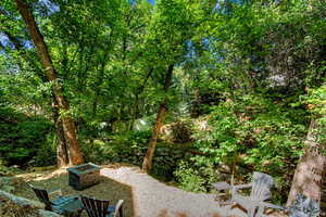 Secluded outdoor area featuring a gravel patio, mature trees, a built-in stone fire pit, and terraced landscaping