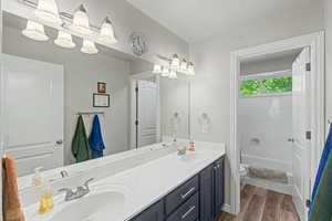 Bathroom featuring a dual vanity with a white countertop and dark cabinetry, wood-finish flooring, a full mirror, and a bathtub with an overhead window