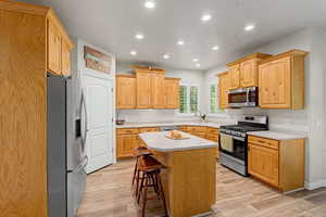 Kitchen featuring wood cabinetry, stainless steel appliances, a center island with seating, recessed lighting, and wood-finish flooring