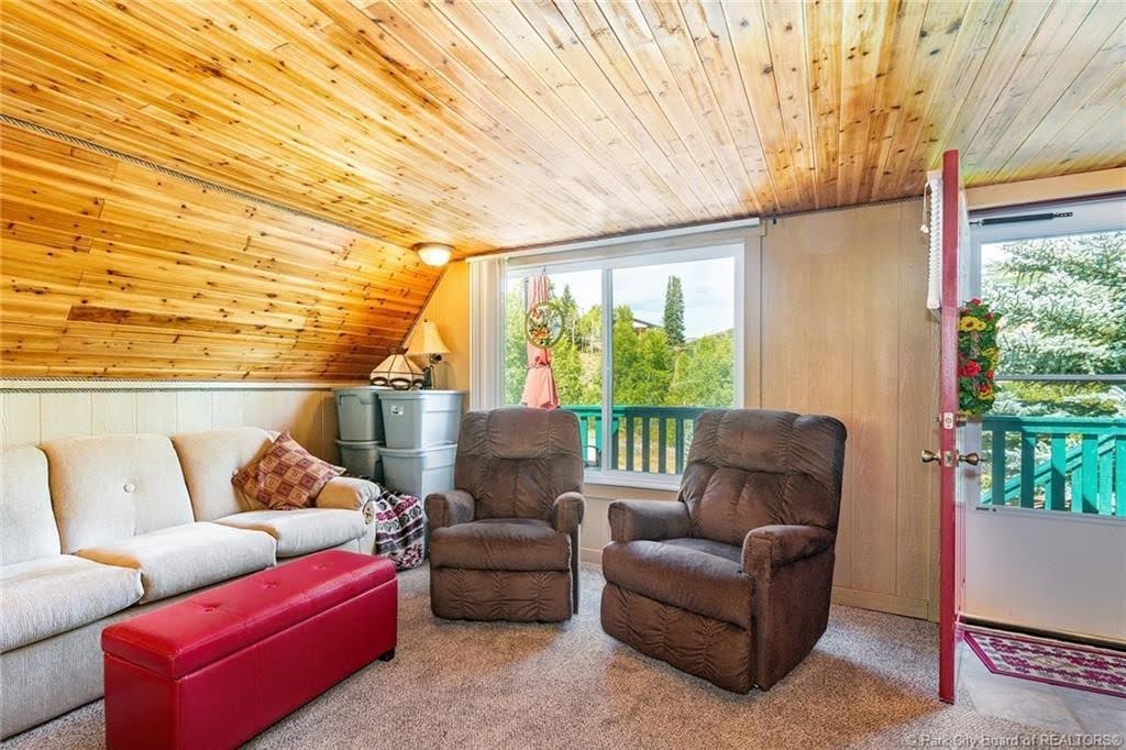 Vaulted wood-paneled ceiling with recessed lighting, carpeted flooring, and a large window overlooking a wooden deck