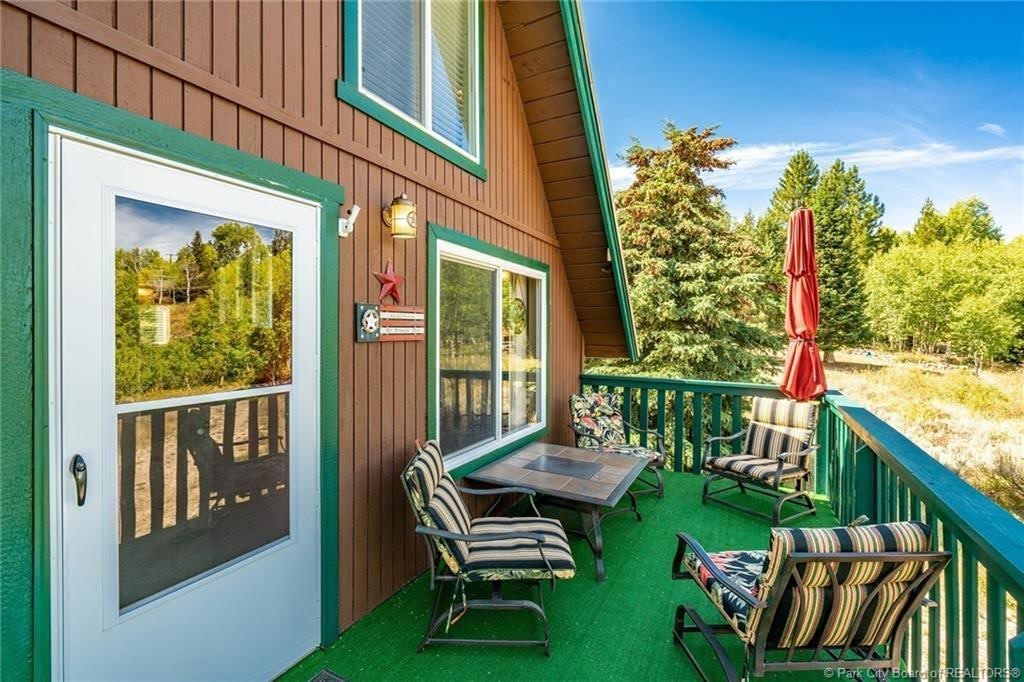 Expansive exterior deck featuring a green-painted railing, green turf flooring, and a brown vertical siding facade with green trim
