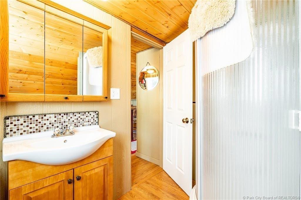 Bathroom featuring a wood-finish ceiling, vanity with integrated basin sink, mosaic tile backsplash, and a mirrored medicine cabinet