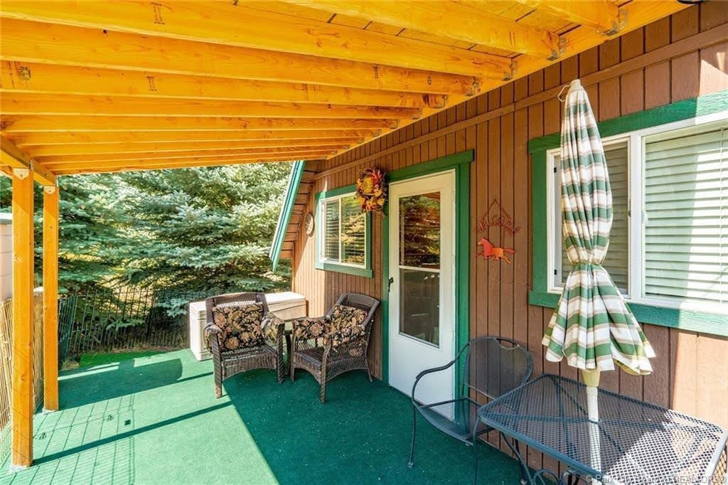 Covered outdoor patio featuring a wooden beam ceiling, green turf flooring, and a brown vertical plank exterior