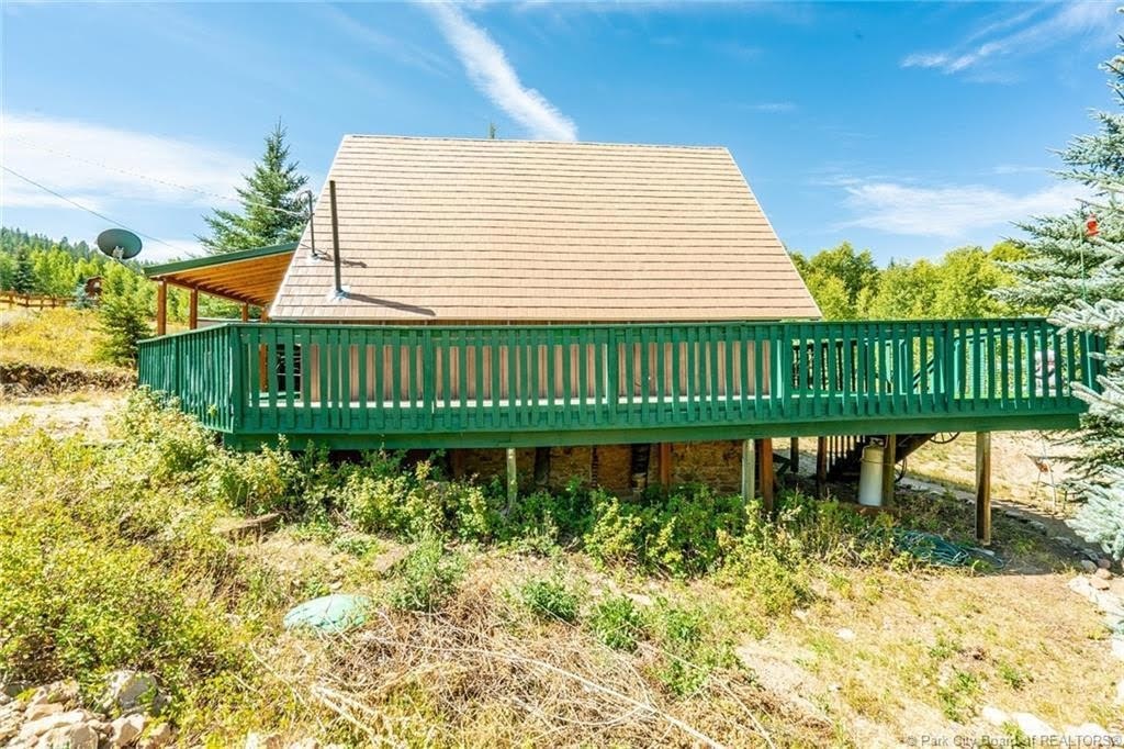Elevated outdoor deck with green railing and slatted privacy screen, featuring a covered patio extension with wood ceiling and exposed beams