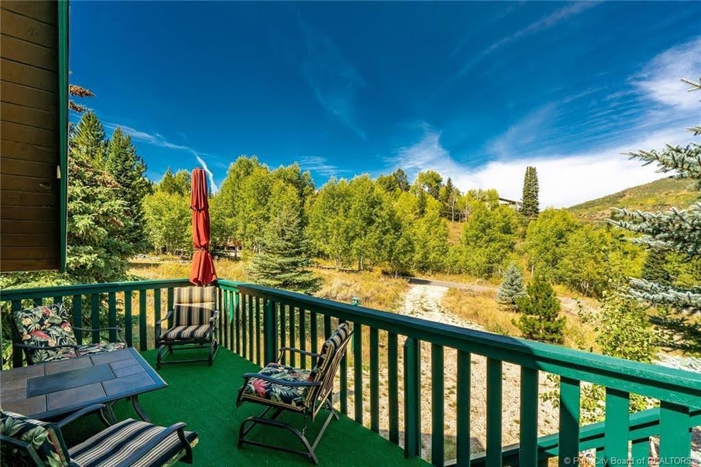 Outdoor deck featuring green railing, artificial turf flooring, and a backdrop of mature trees and a distant hillside