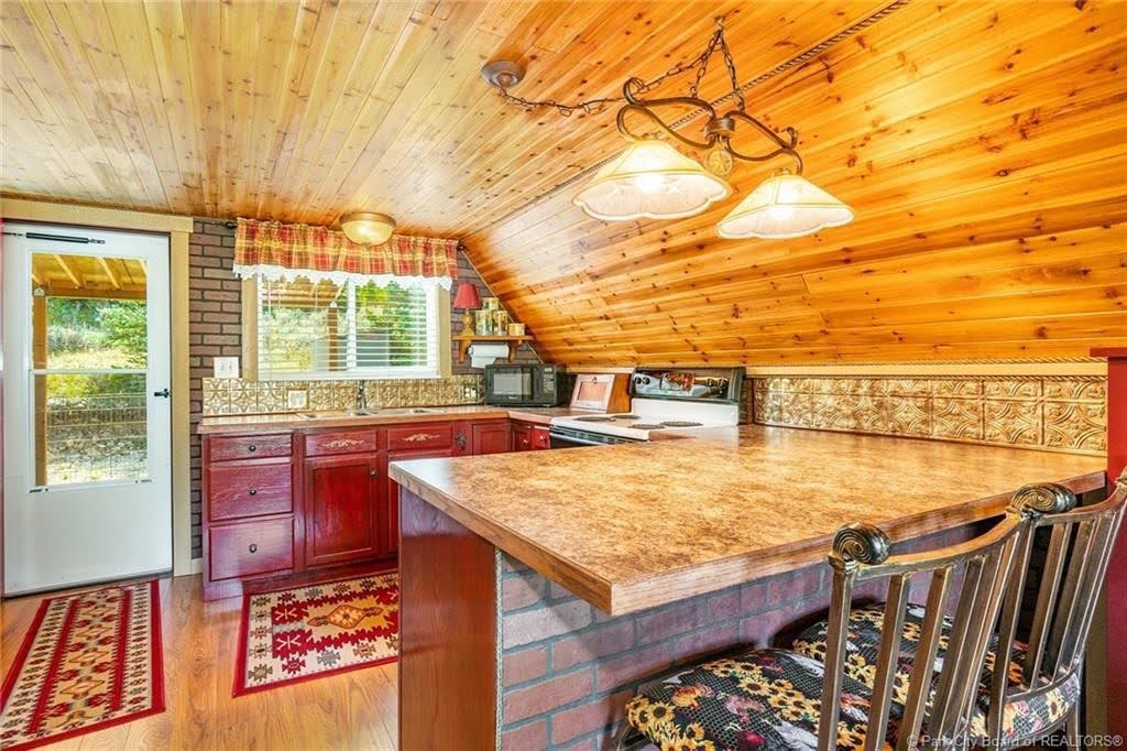 Kitchen featuring wood-finish flooring, wood plank ceiling, red cabinetry, brick accents, and a built-in kitchen island with stone-look countertop