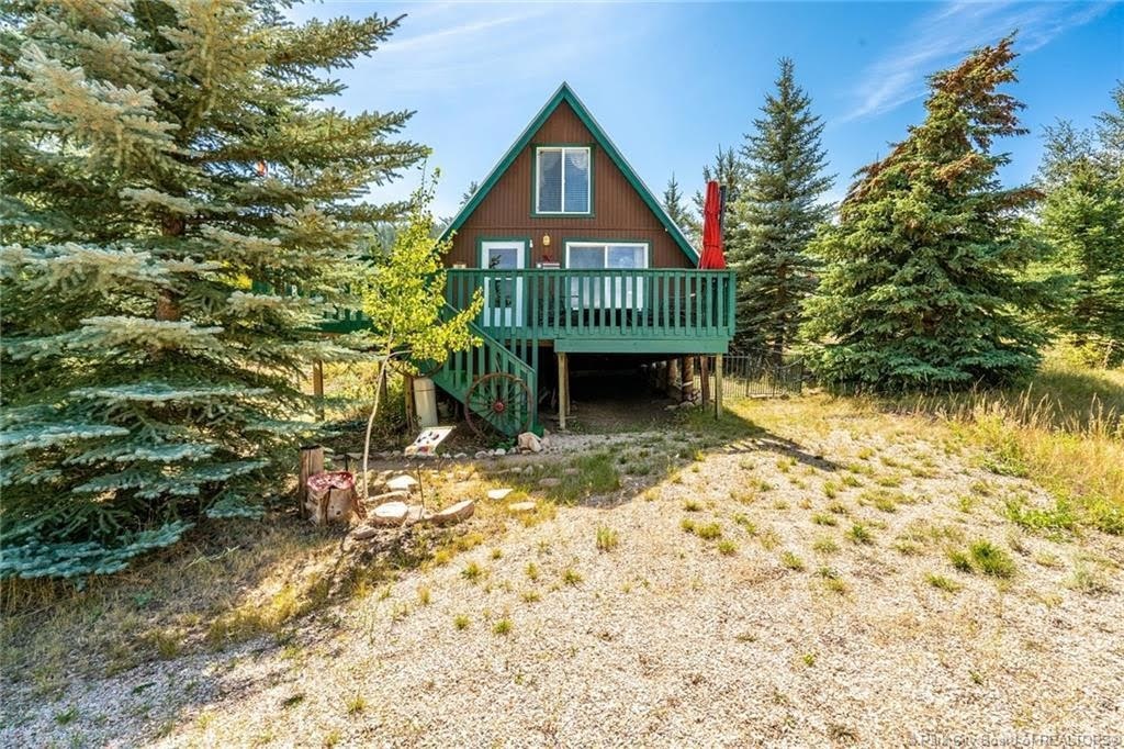 A-frame exterior with a brown façade and green trim, featuring an elevated deck with matching green railings, and a stairway with stone risers