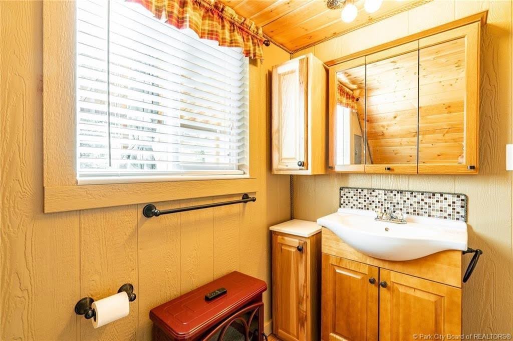 Bathroom featuring a wood-panel accent ceiling and walls, a light wood vanity with a white vessel sink, a mosaic tile backsplash, and a mirrored medicine cabinet