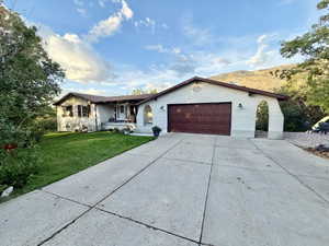 Ranch-style exterior with a split-level design, featuring a two-car garage with an arched entryway, a concrete driveway, a manicured lawn, and mature landscaping
