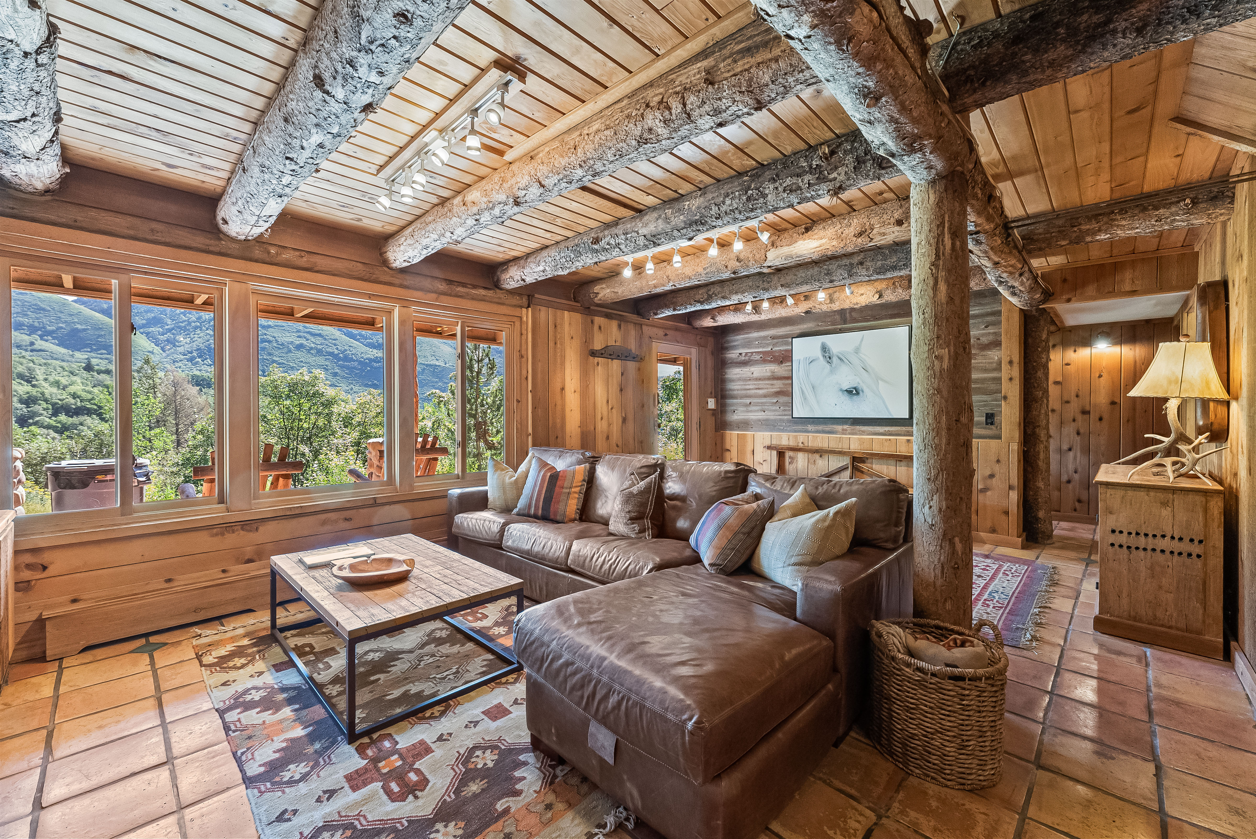 Rustic living area featuring exposed log beams, wood plank ceilings, and paneled walls