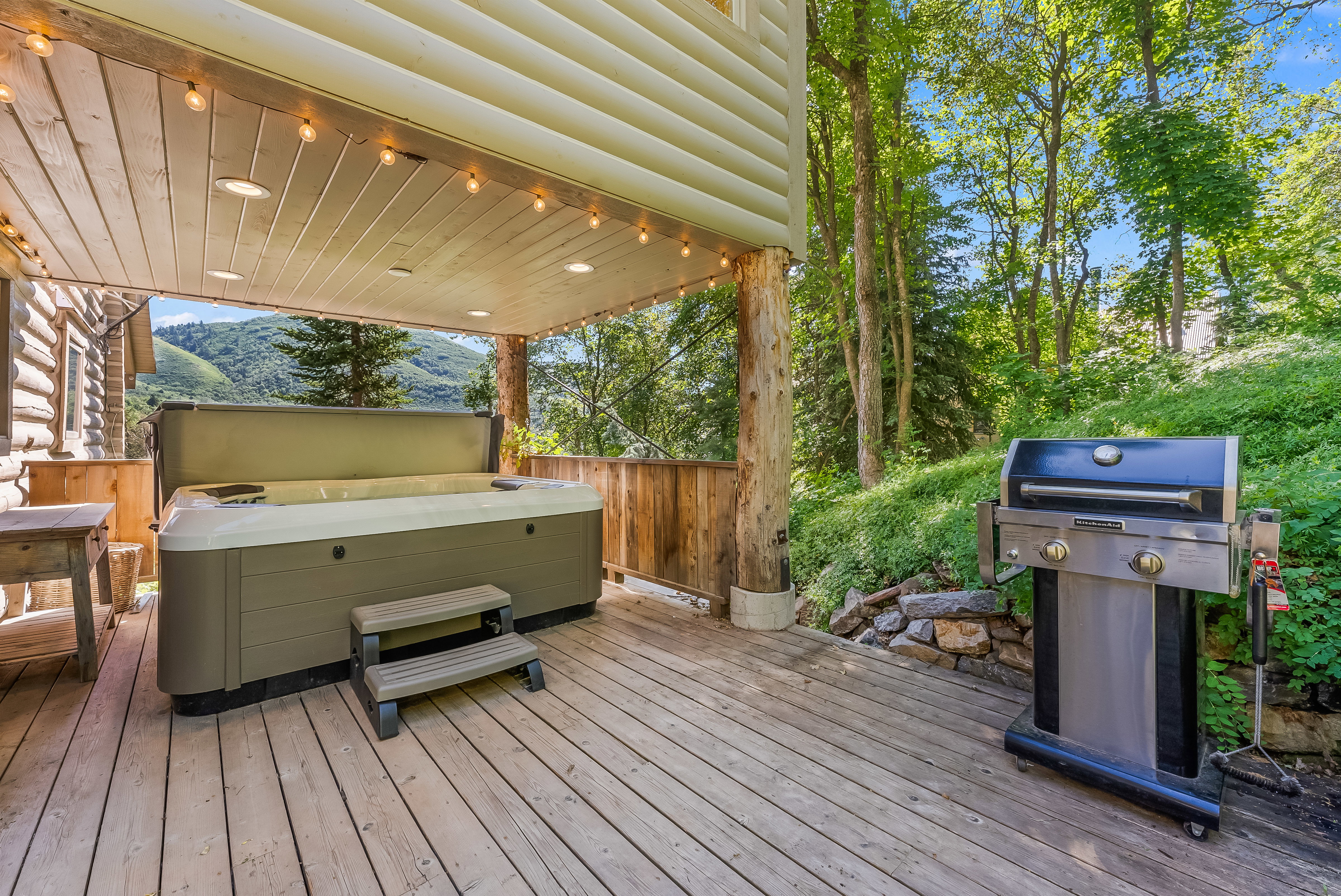 Expansive wood-finish deck featuring a built-in spa, overhead string lighting, recessed ceiling lights, and wooden railings