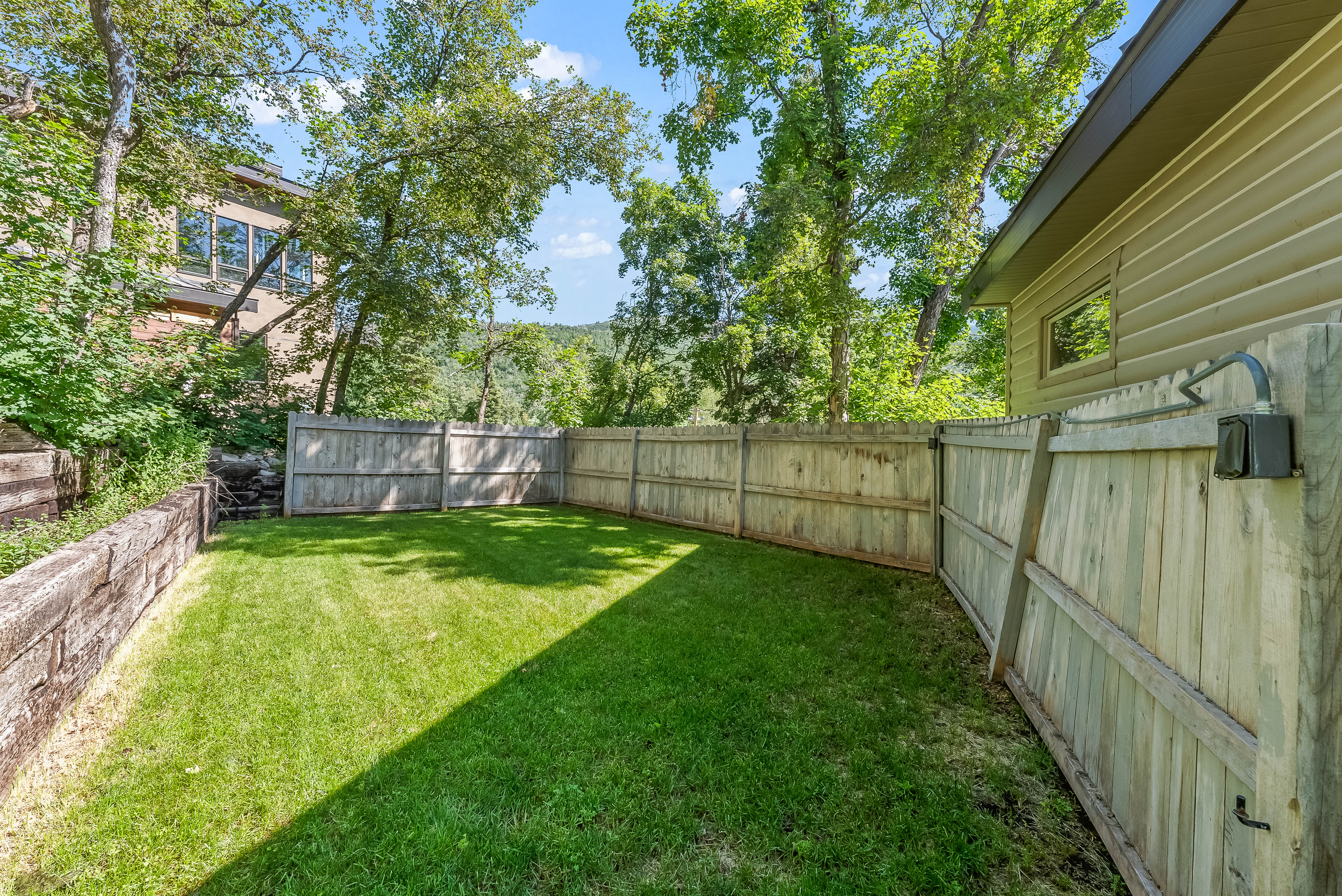 Private backyard featuring a manicured lawn, full perimeter wood fencing, and a built-in timber retaining wall