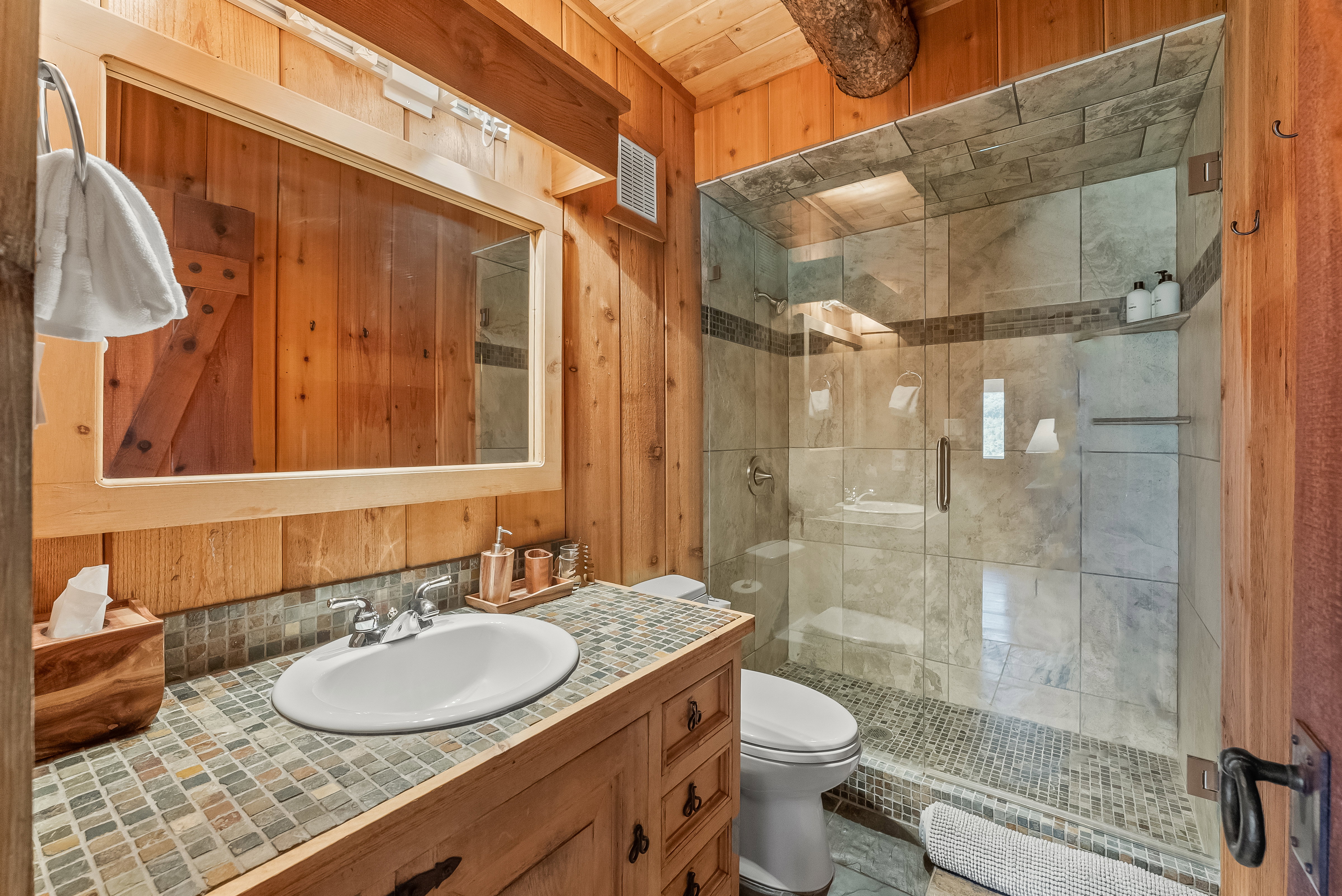 Wood-paneled bathroom featuring a glass-enclosed shower with tile surround and stone flooring