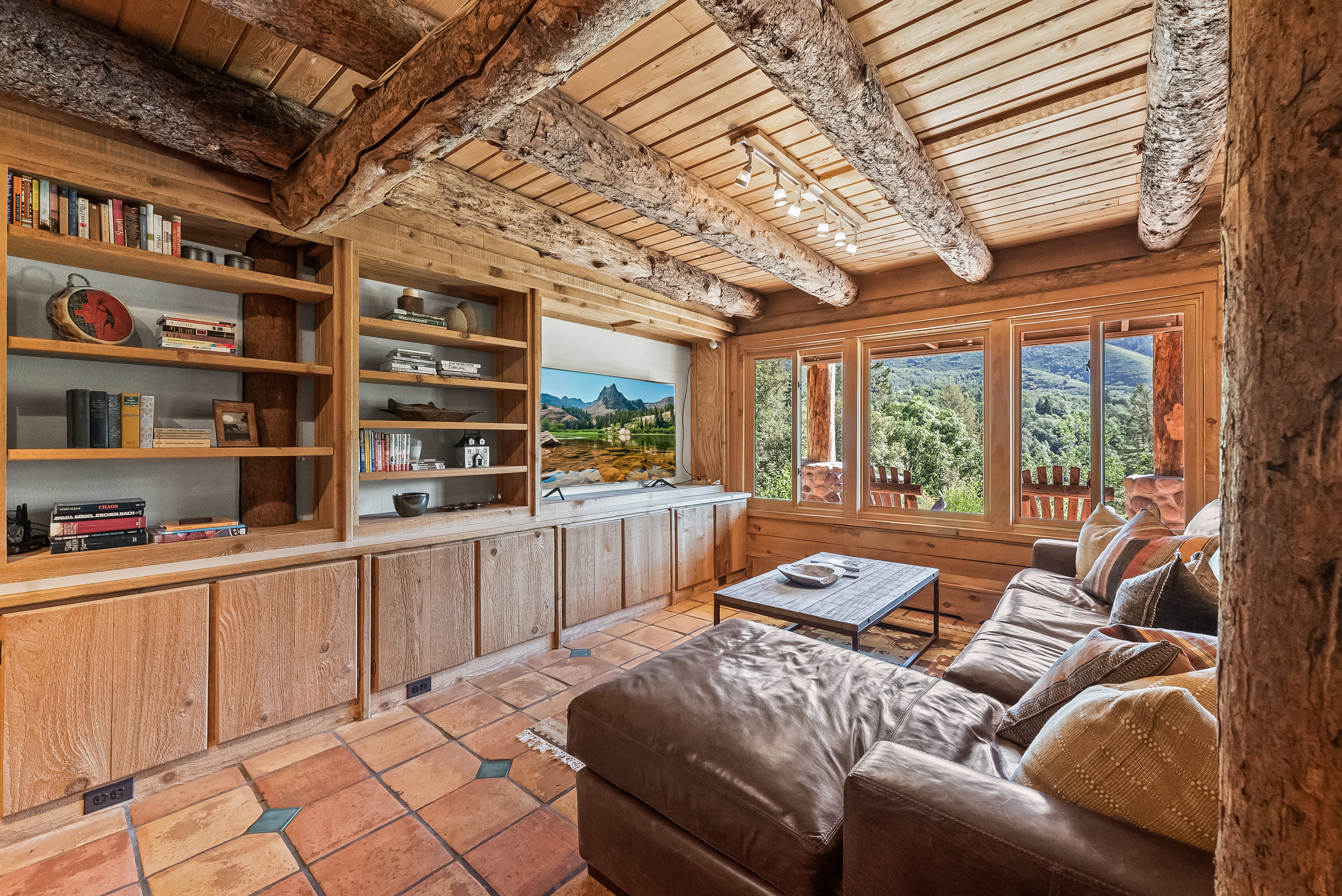 Rustic living area featuring exposed log beams, wood-planked ceilings, and a built-in entertainment center with open shelving and cabinet storage