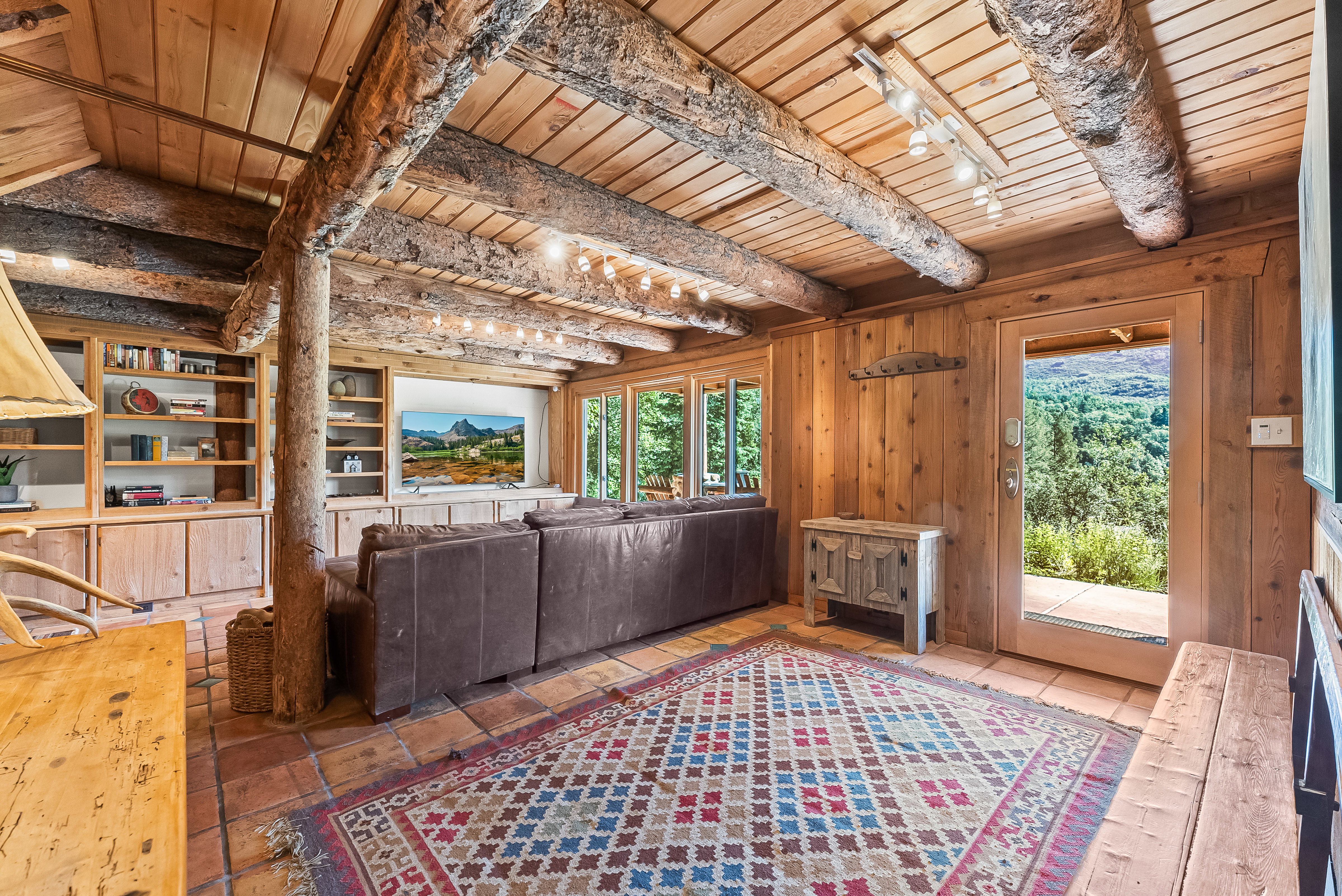 Living area featuring rustic wood beam ceilings, wood-finish walls, and terracotta tile flooring