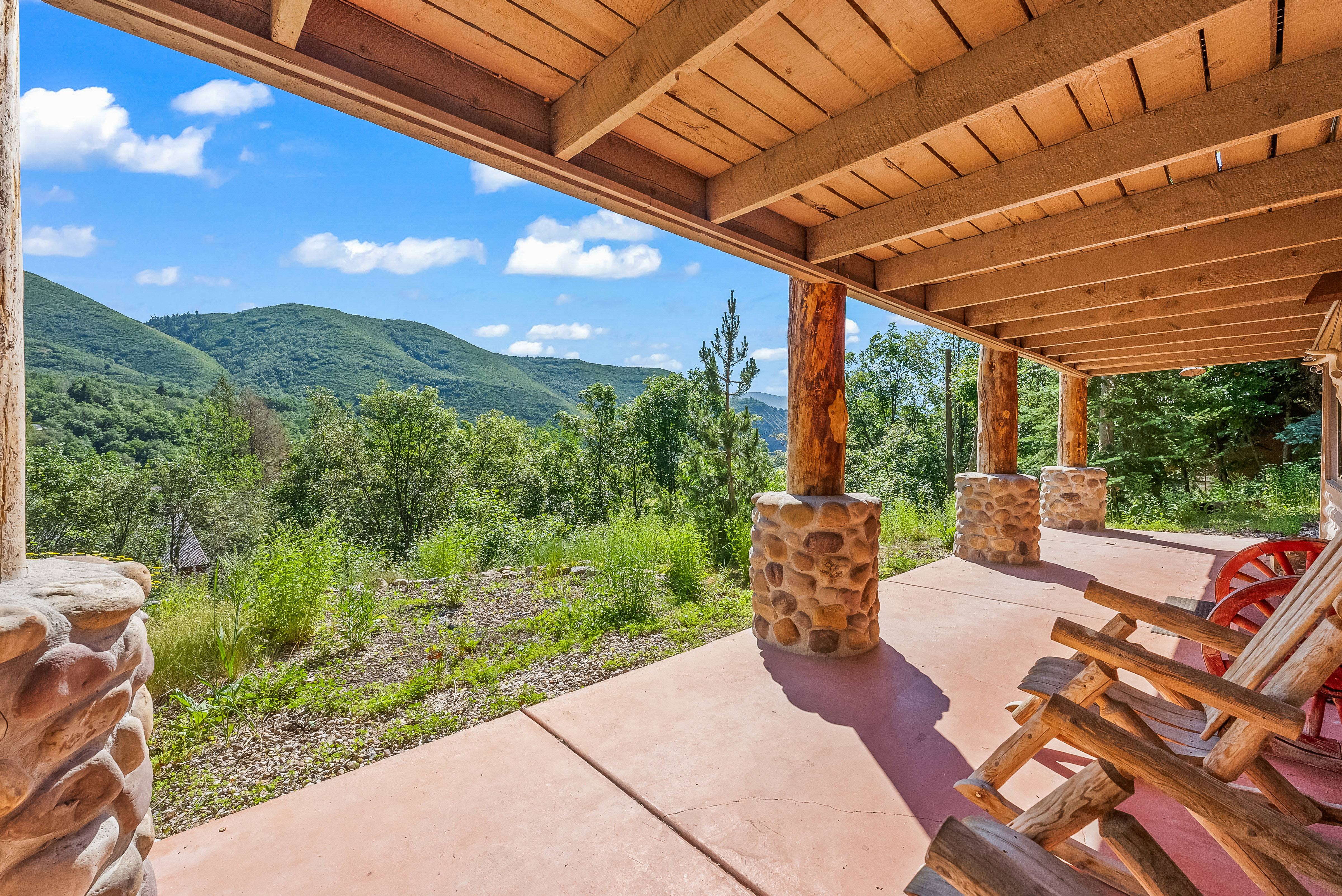Covered patio featuring a concrete floor, stone pillar bases, and natural wood beams
