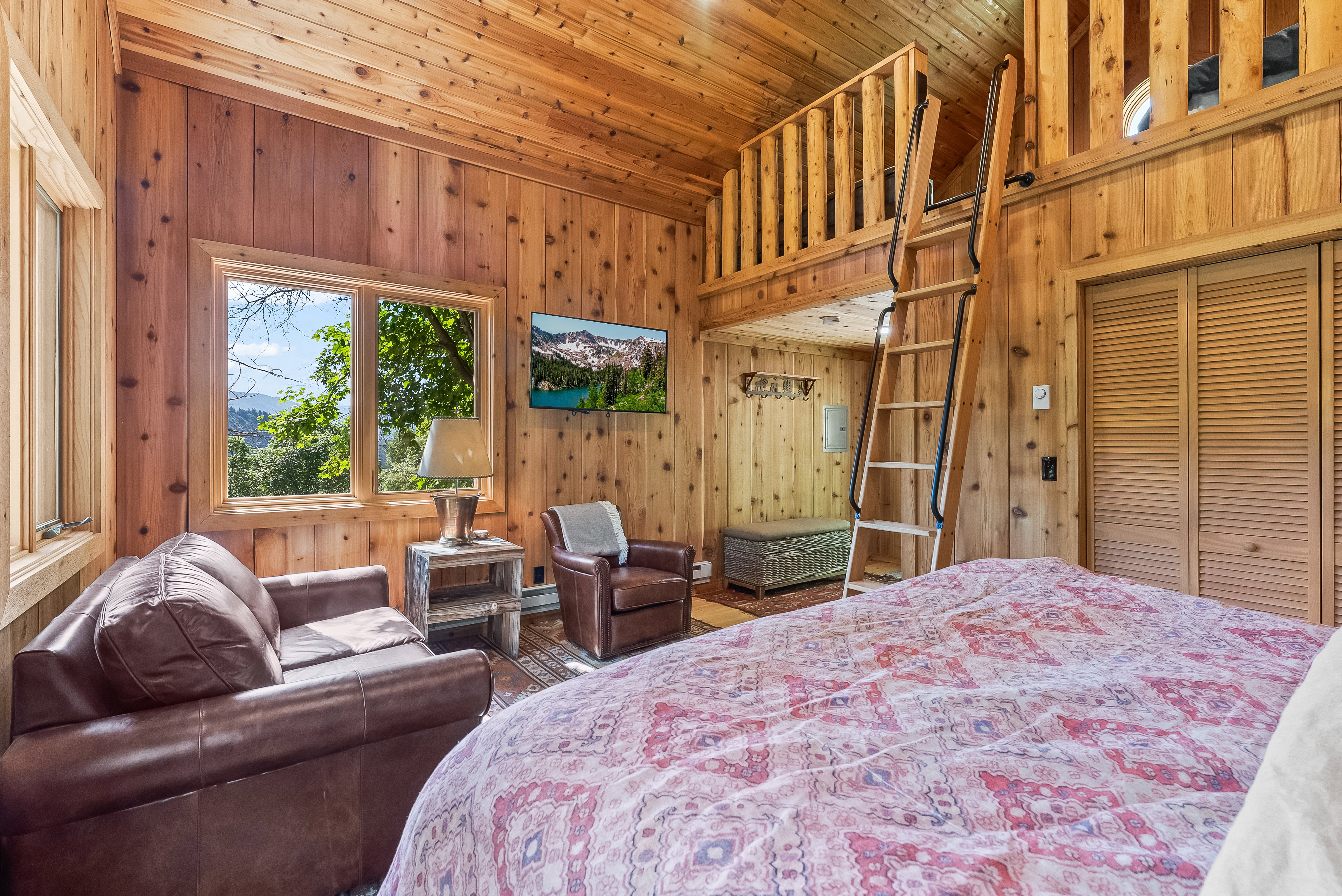Interior featuring extensive wood paneling and wood-finish ceiling, multiple windows, a built-in loft with wood railing, and a wood ladder for access
