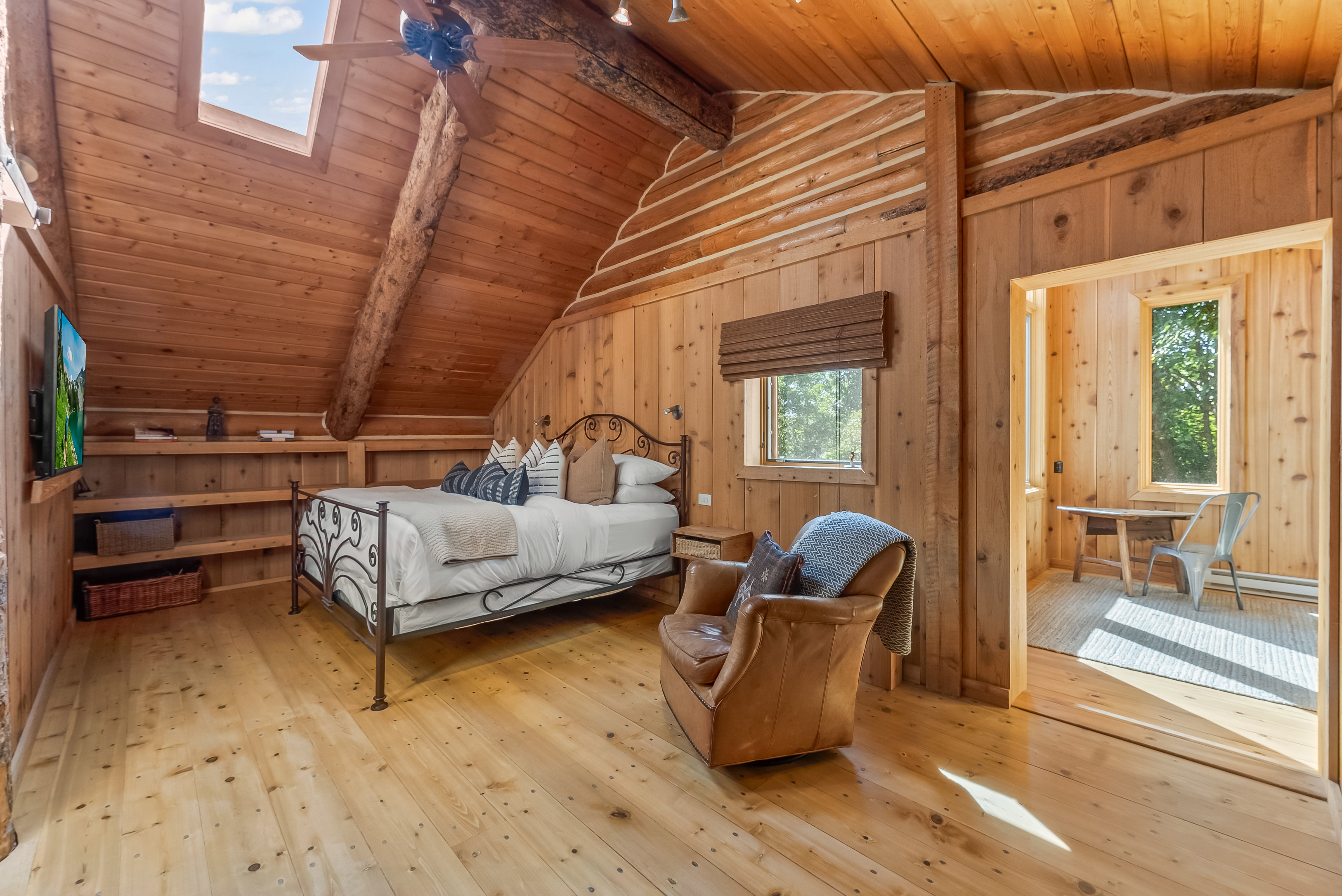Wood-paneled room featuring natural wood flooring and an angled wood-plank ceiling with a skylight