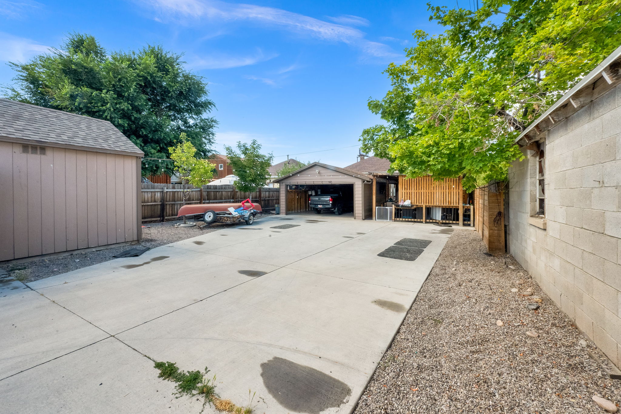 Expansive concrete pad providing ample off-street parking, accompanied by a detached shed with a shingled roof, a detached garage, and an additional block construction outbuilding