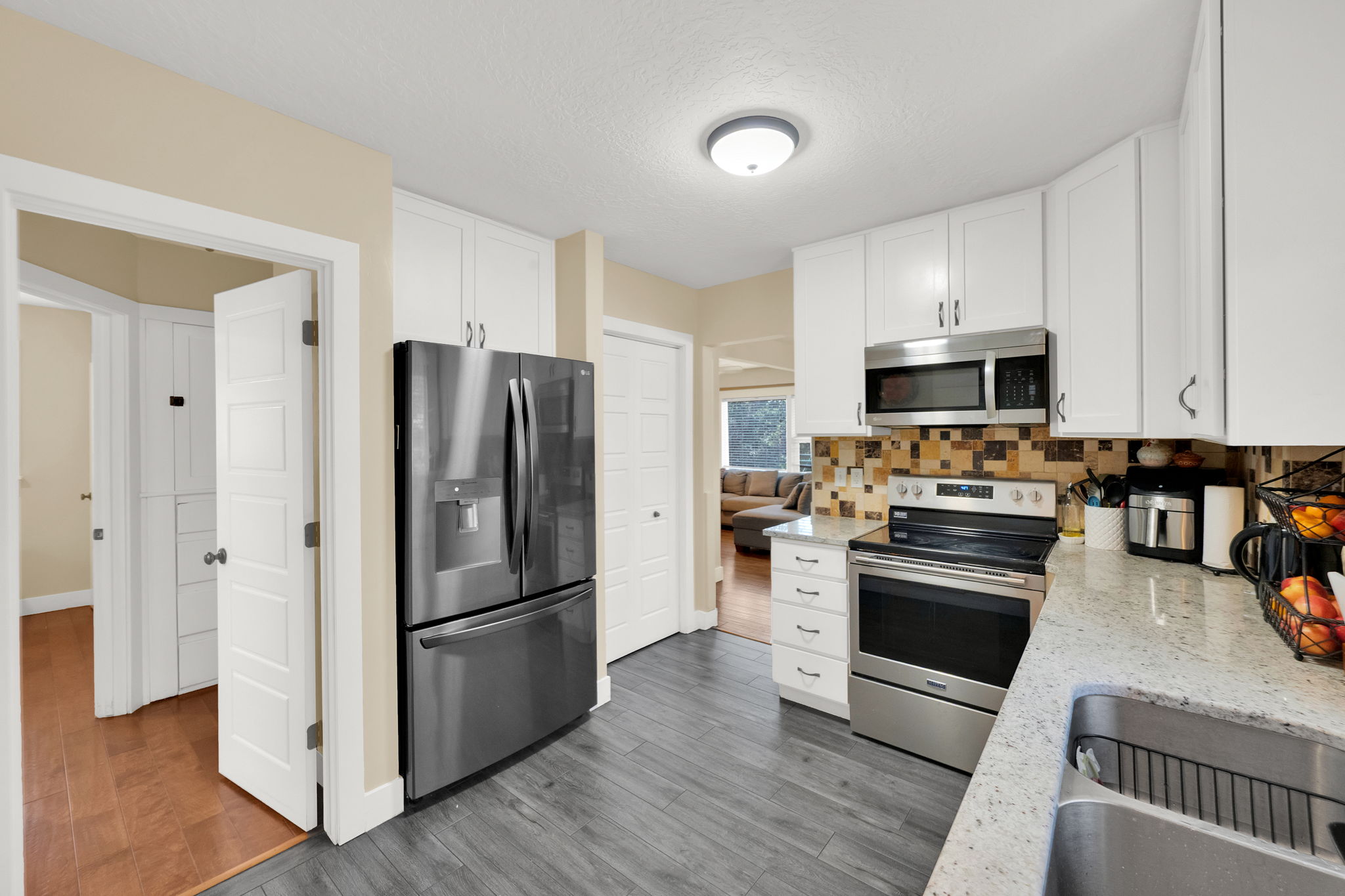 Kitchen featuring wood-finish flooring, white cabinetry, stainless steel appliances, a multi-tone tile backsplash, and light-toned countertops
