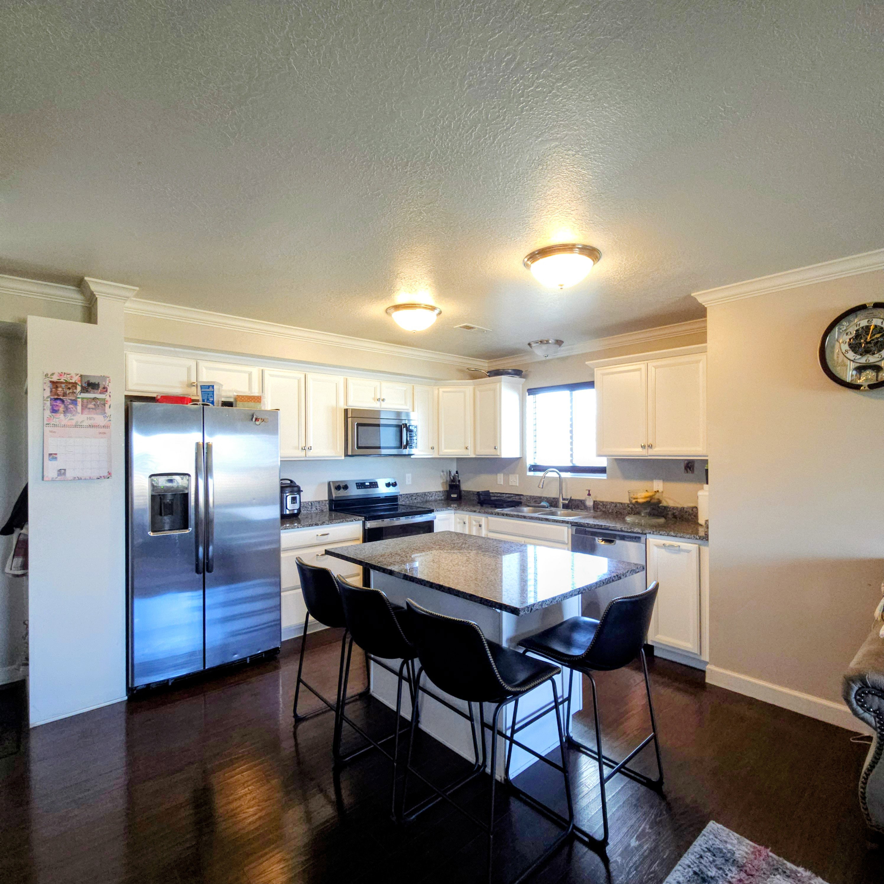 Well-appointed kitchen featuring white cabinetry, dark wood-finish flooring, a central island with countertop seating, stainless steel appliances, and crown molding accents
