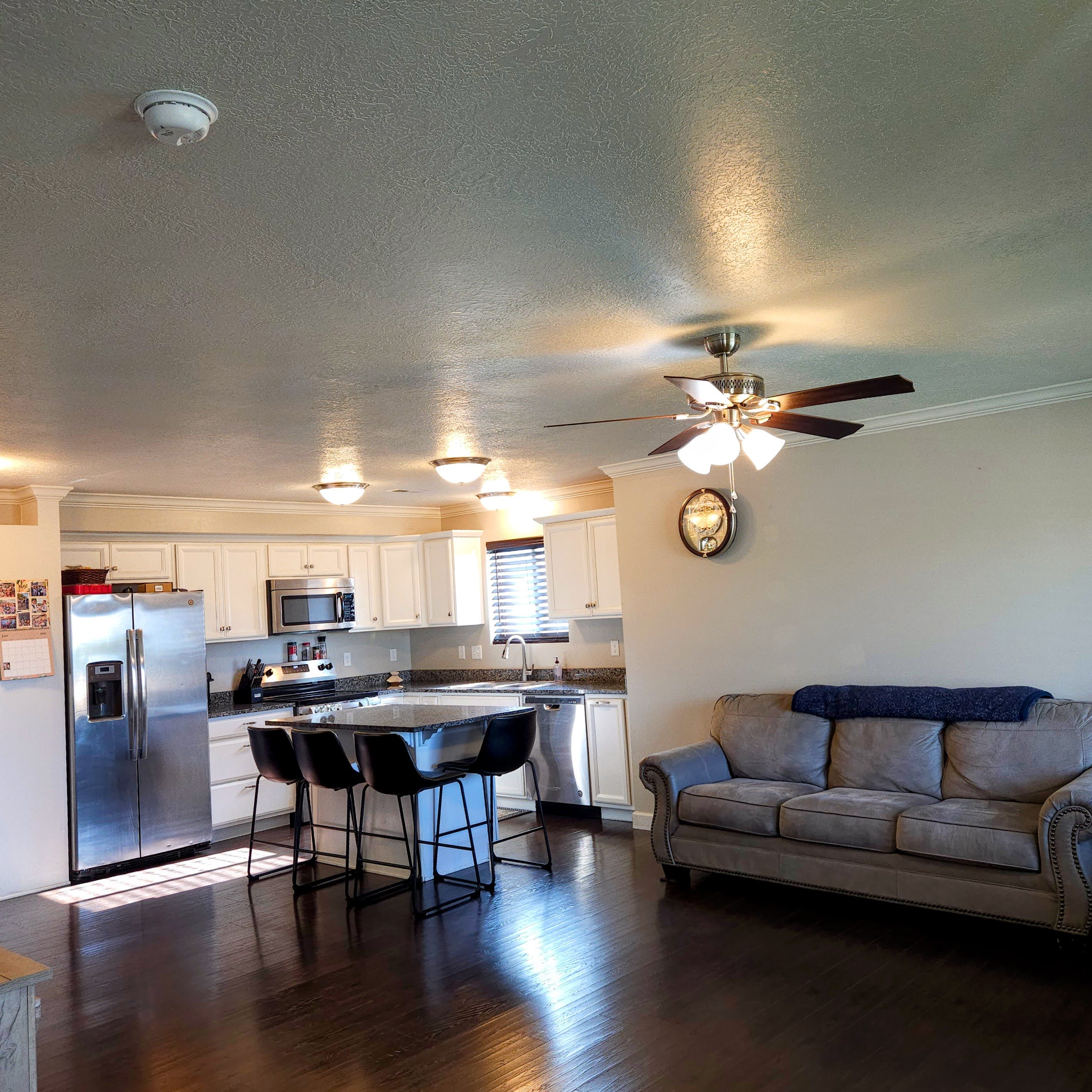 Open-concept living space featuring wood-finish flooring, a kitchen island with seating, stainless steel appliances, white cabinetry, and a ceiling fan