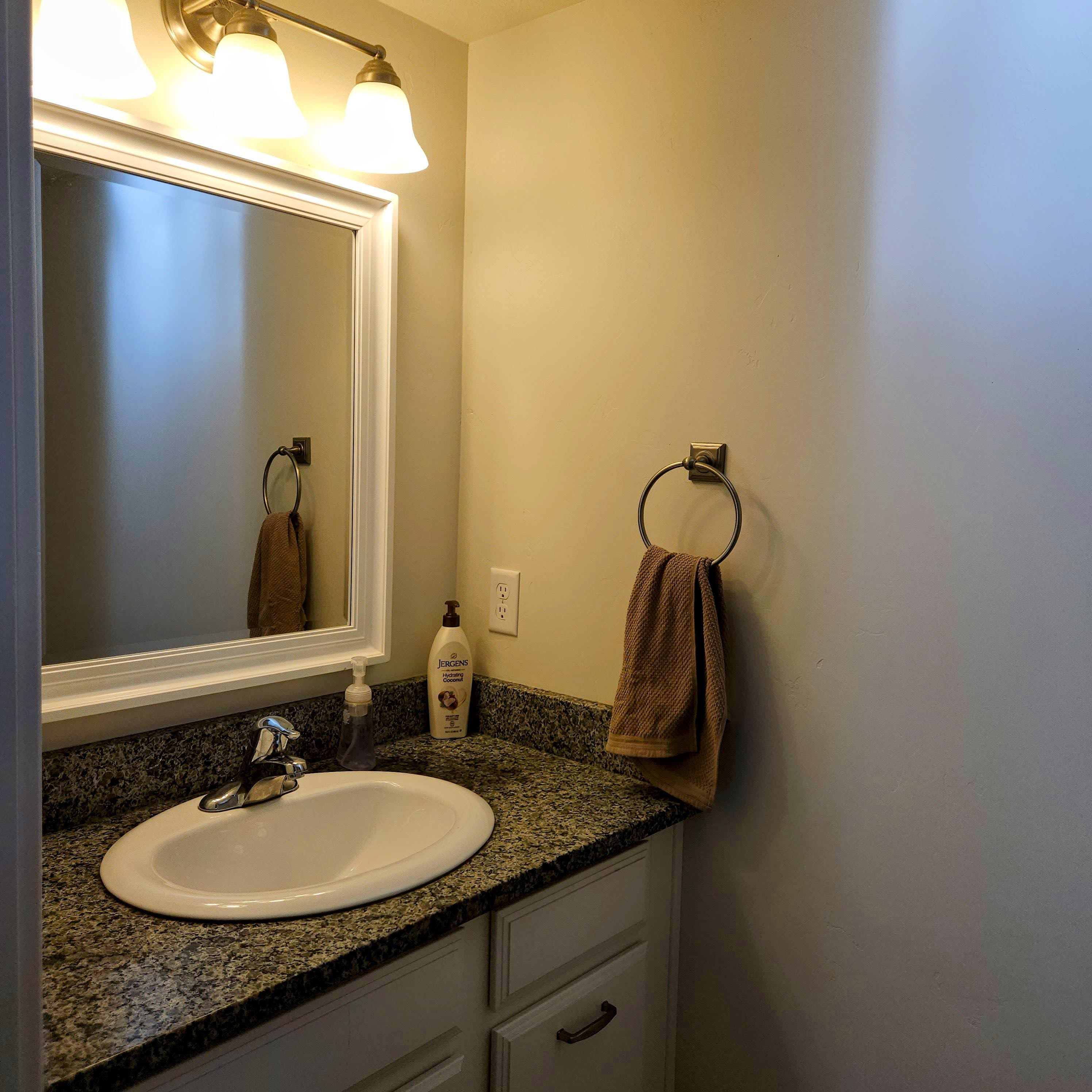 Bathroom vanity featuring a granite-style countertop, undermount sink, and white cabinetry with dark hardware