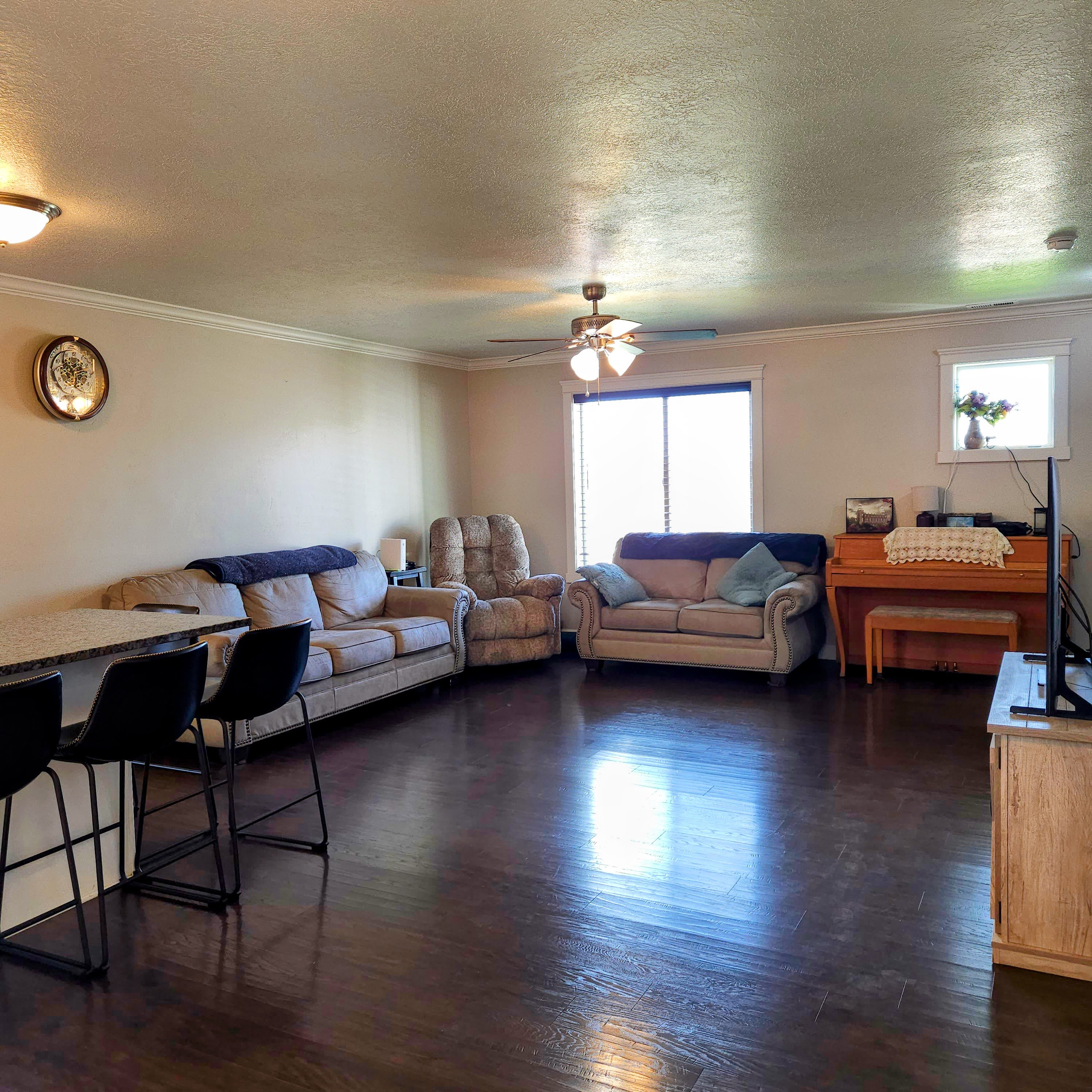 Spacious living area featuring dark wood-finish flooring, crown molding, and a ceiling fan with integrated lighting