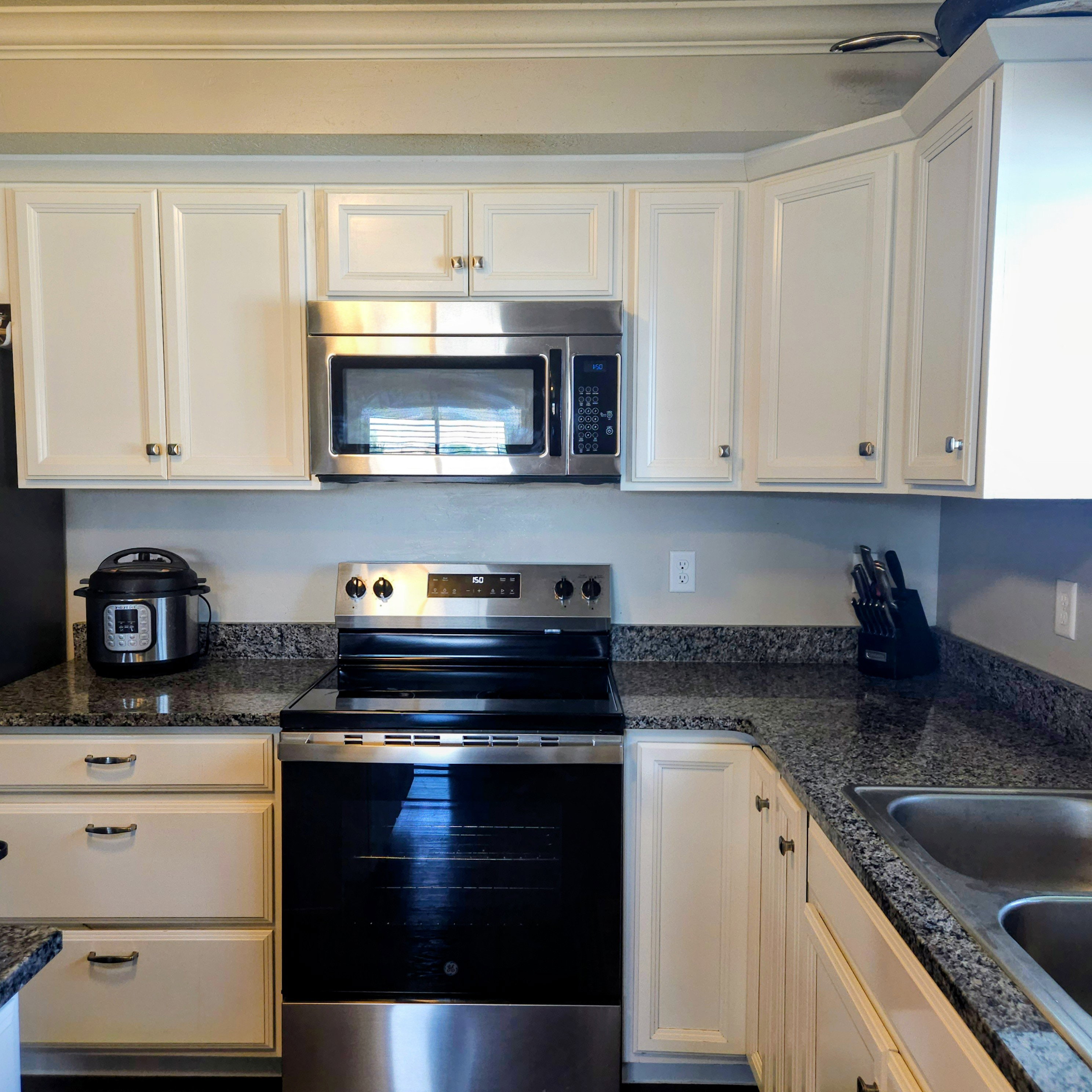 Kitchen featuring white cabinetry, granite-finish countertops, stainless steel appliances, an over-the-range microwave, and a double basin sink