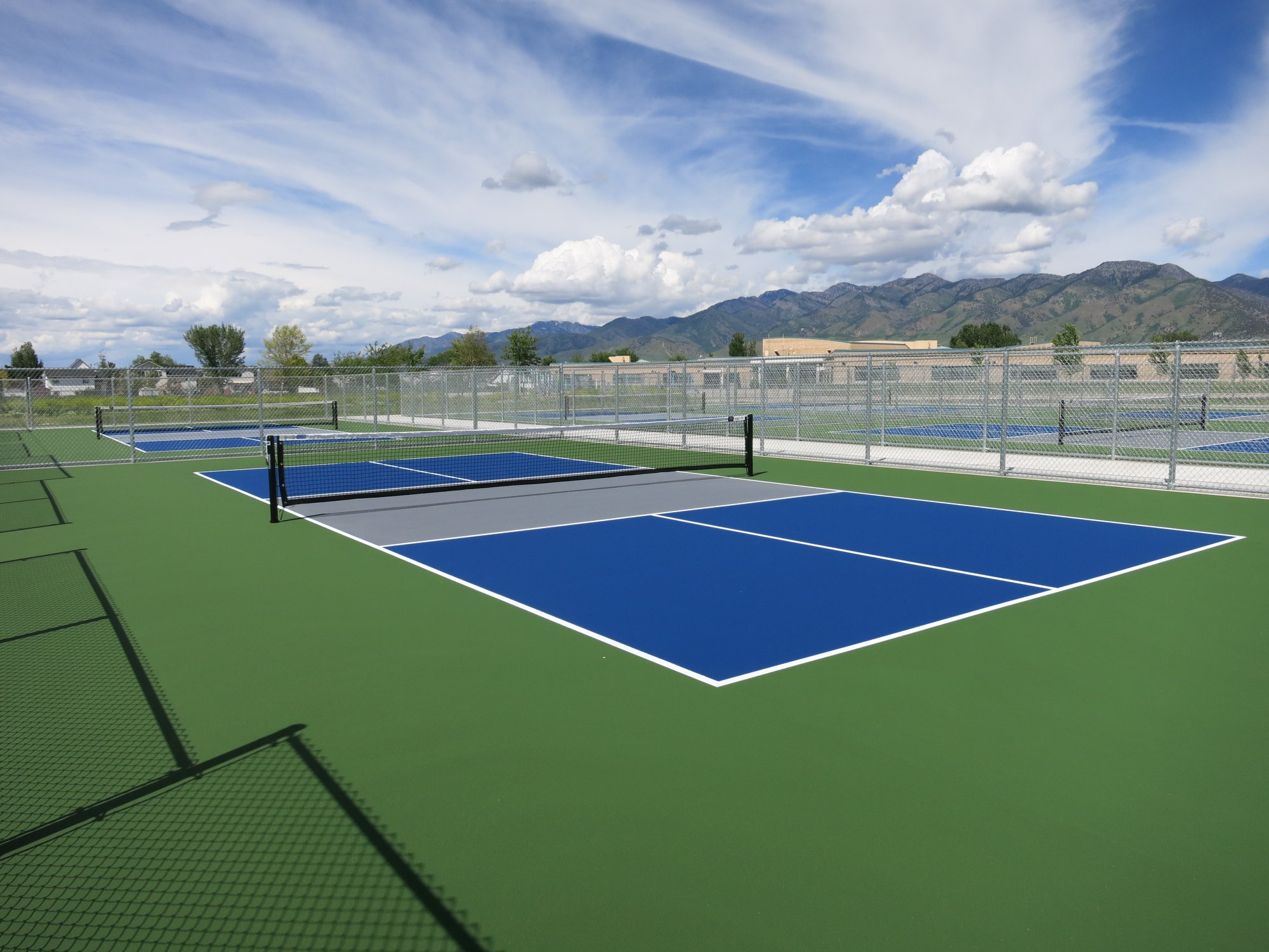 Multiple courts featuring blue and gray playing surfaces with white boundary lines