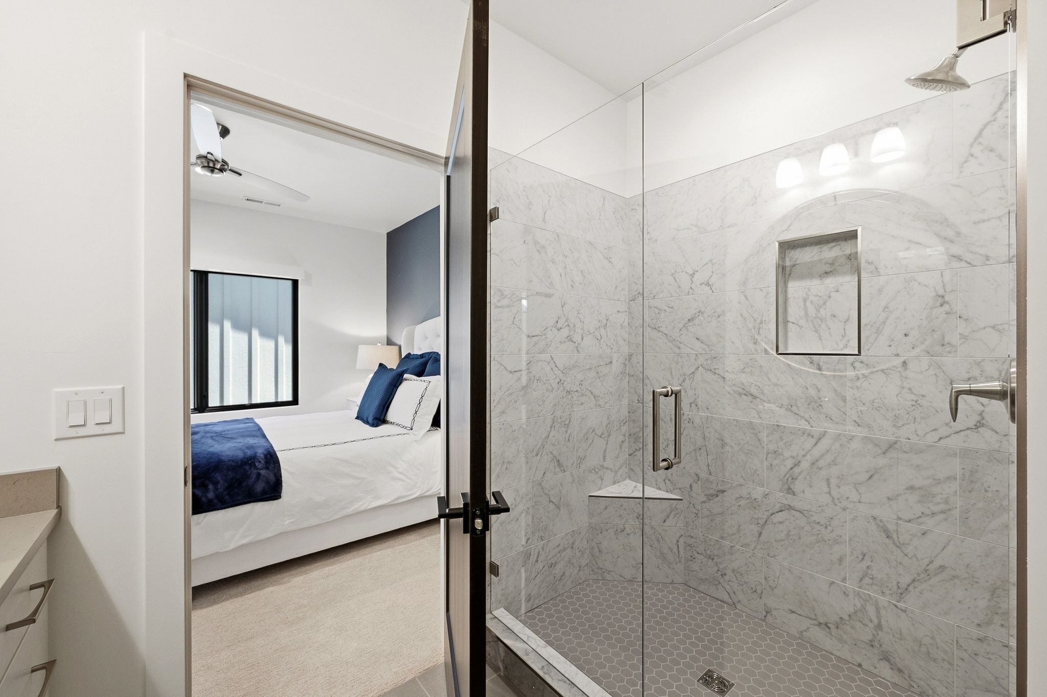 Glass-enclosed shower with large format tile surround, hexagon tile flooring, and integrated shower niche