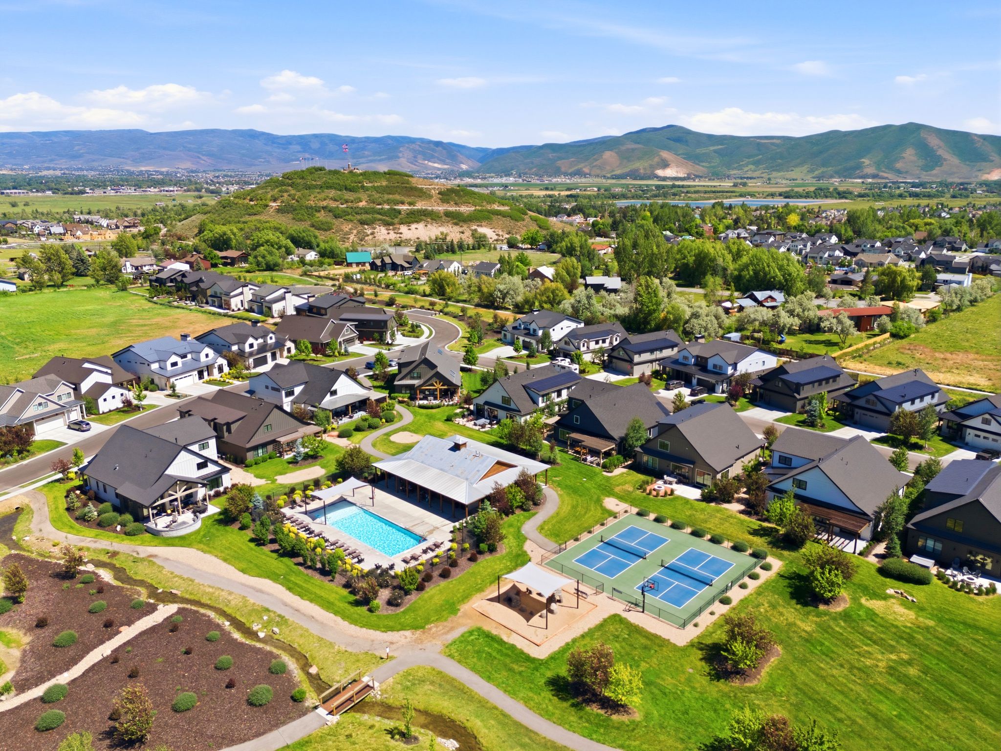 Community featuring residential homes, a recreational pool, multiple sports courts, and walking paths, all set against a backdrop of rolling hills and distant mountains
