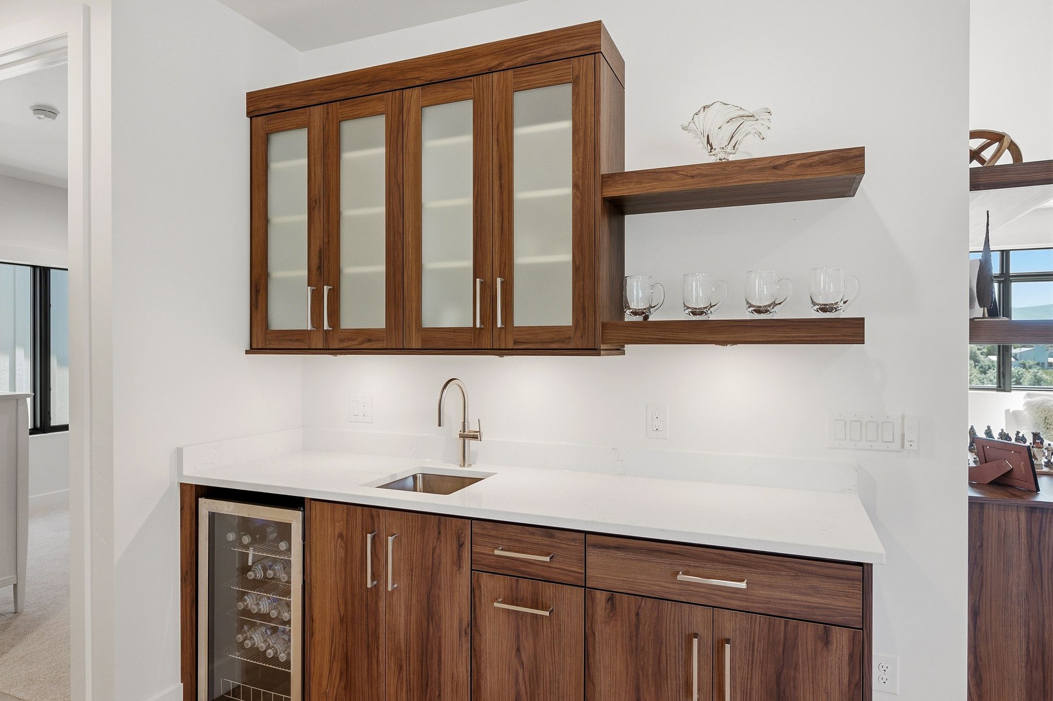 Integrated wet bar featuring rich wood-finish cabinetry, a stainless steel sink, and a built-in beverage cooler