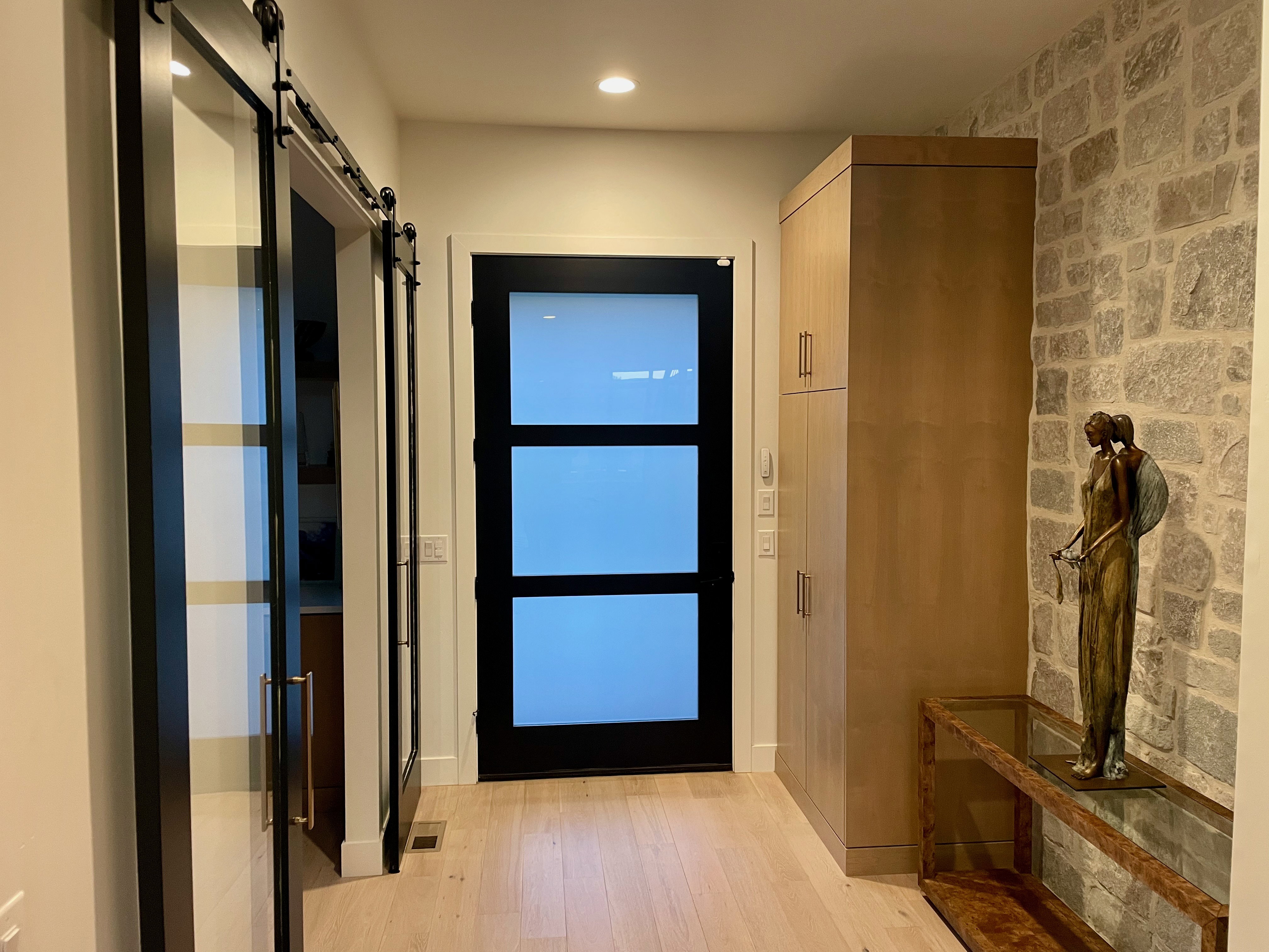 Entryway featuring light wood-finish flooring, a contemporary black door with frosted glass panels, and a stone accent wall