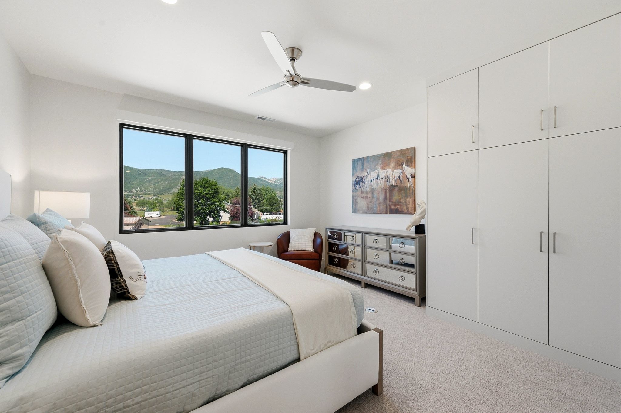 Bright bedroom with large multi-pane window, flush-mounted ceiling lighting, and a ceiling fan