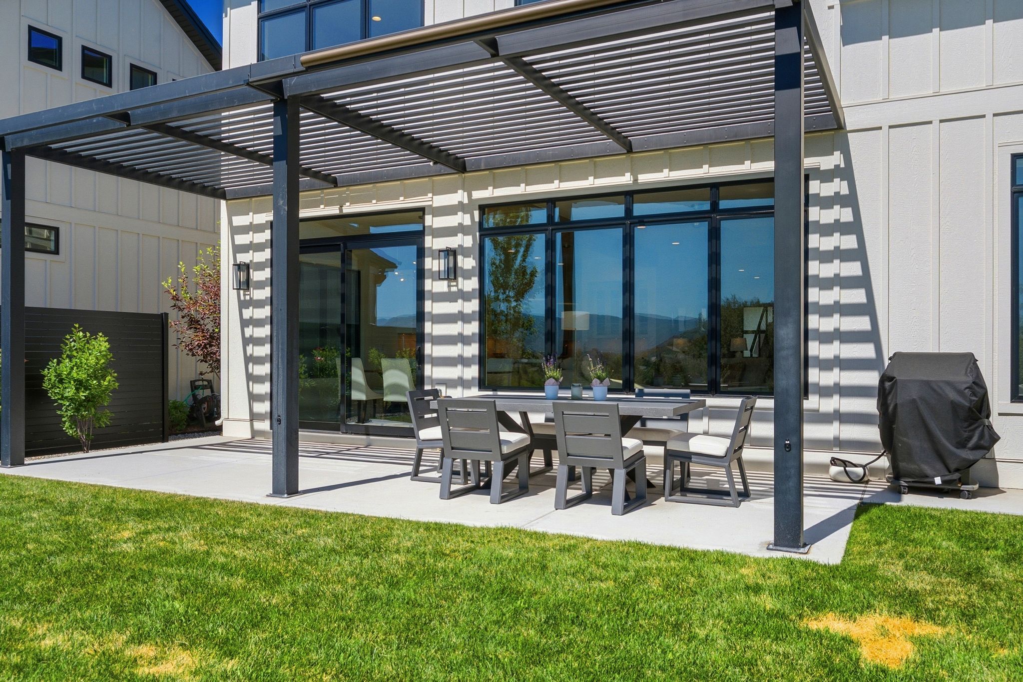 Exterior patio with a black slatted pergola over concrete surfacing