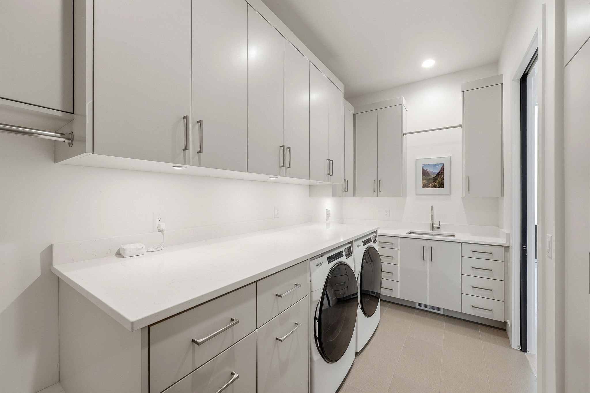 Modern laundry area featuring extensive overhead and base cabinetry, light-toned countertops, and a built-in sink with a gooseneck faucet