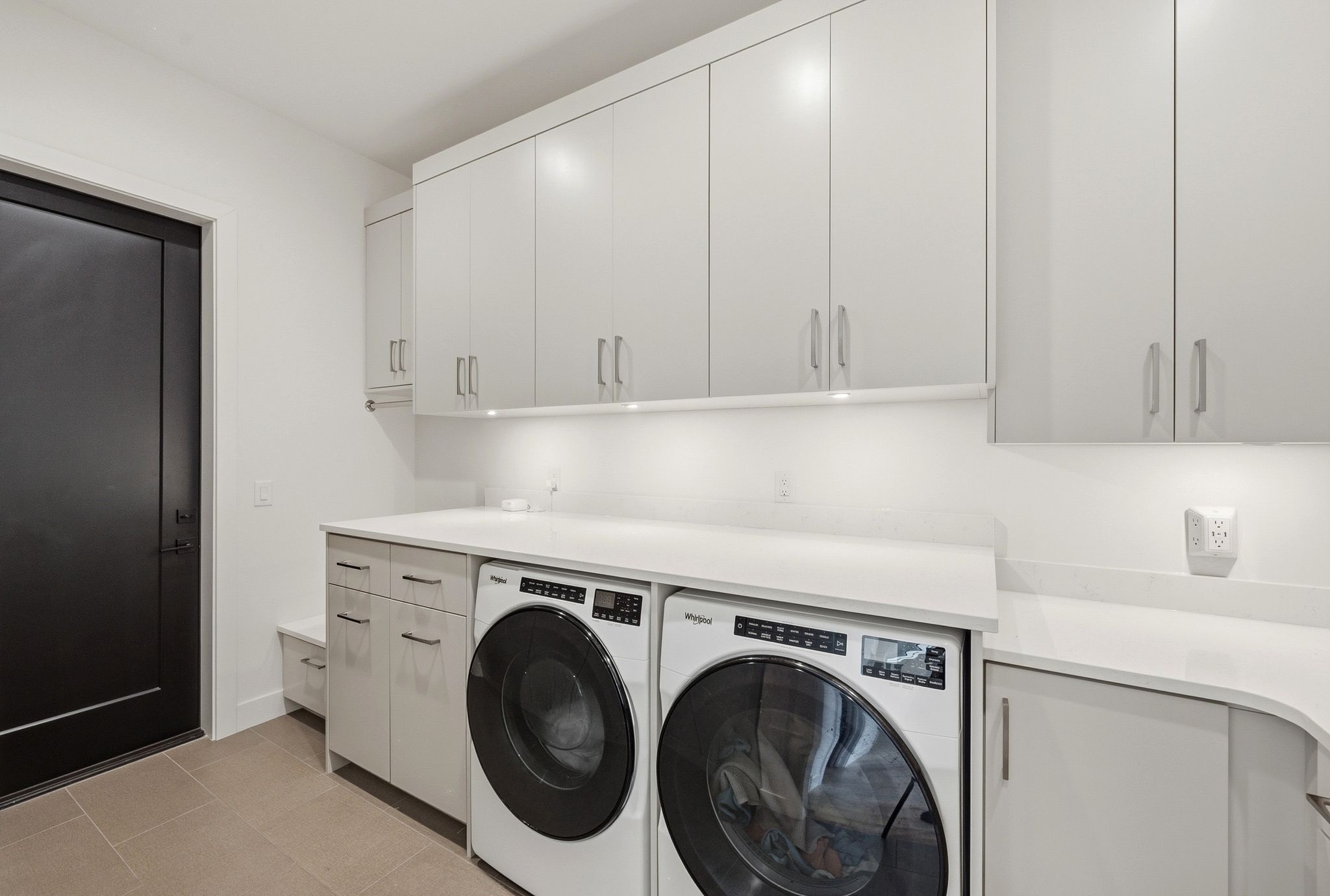 Dedicated laundry space featuring a side-by-side washer and dryer, extensive light gray cabinetry, and a light-toned countertop