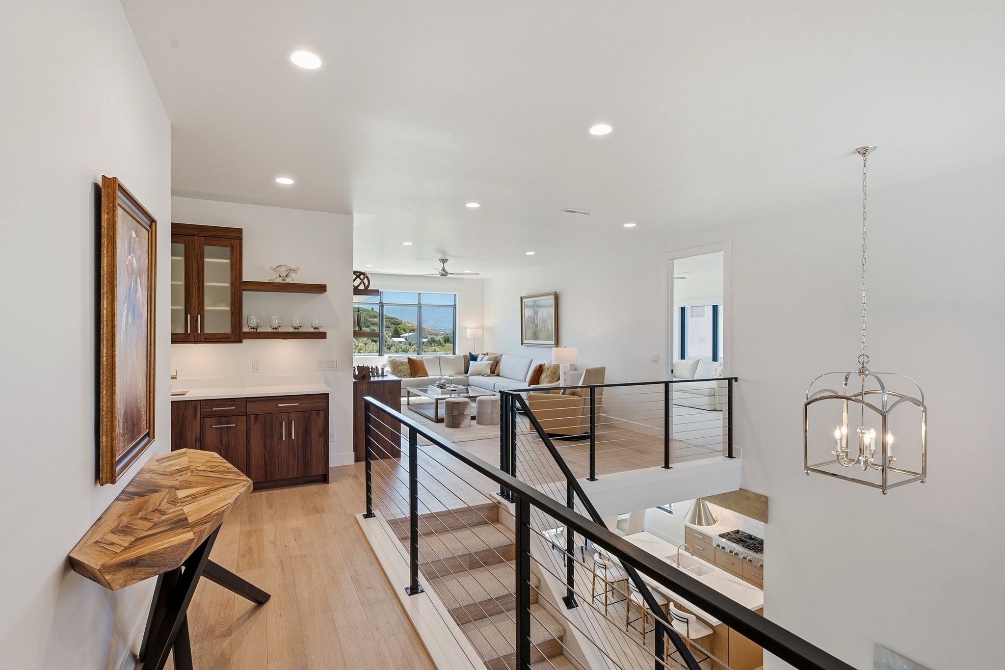 Staircase featuring cable railing and light wood-finish treads, complemented by a built-in wet bar with dark wood cabinetry and floating shelves