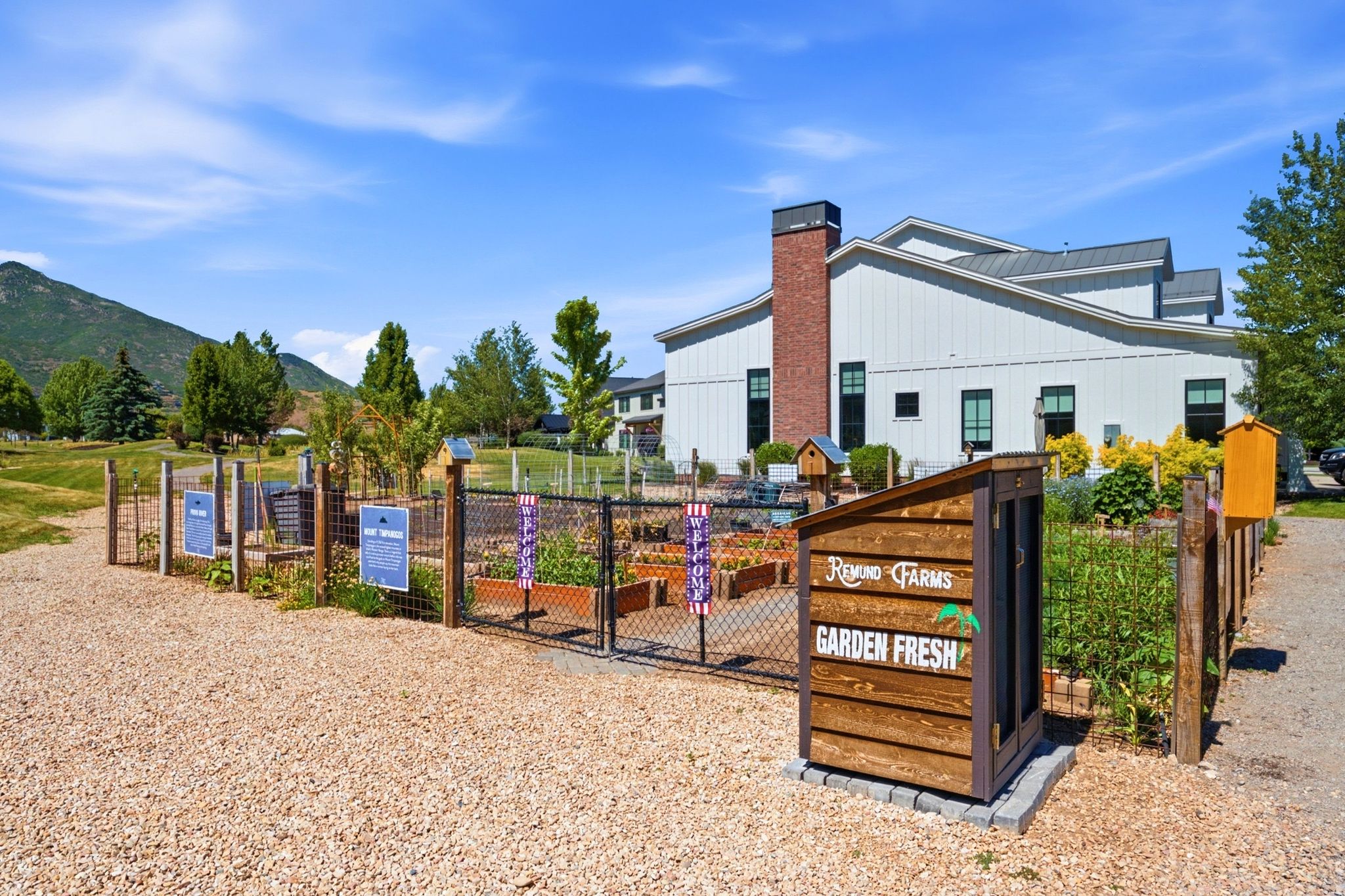 Community garden beds featuring mature plants, wood fencing, and a gravel pathway