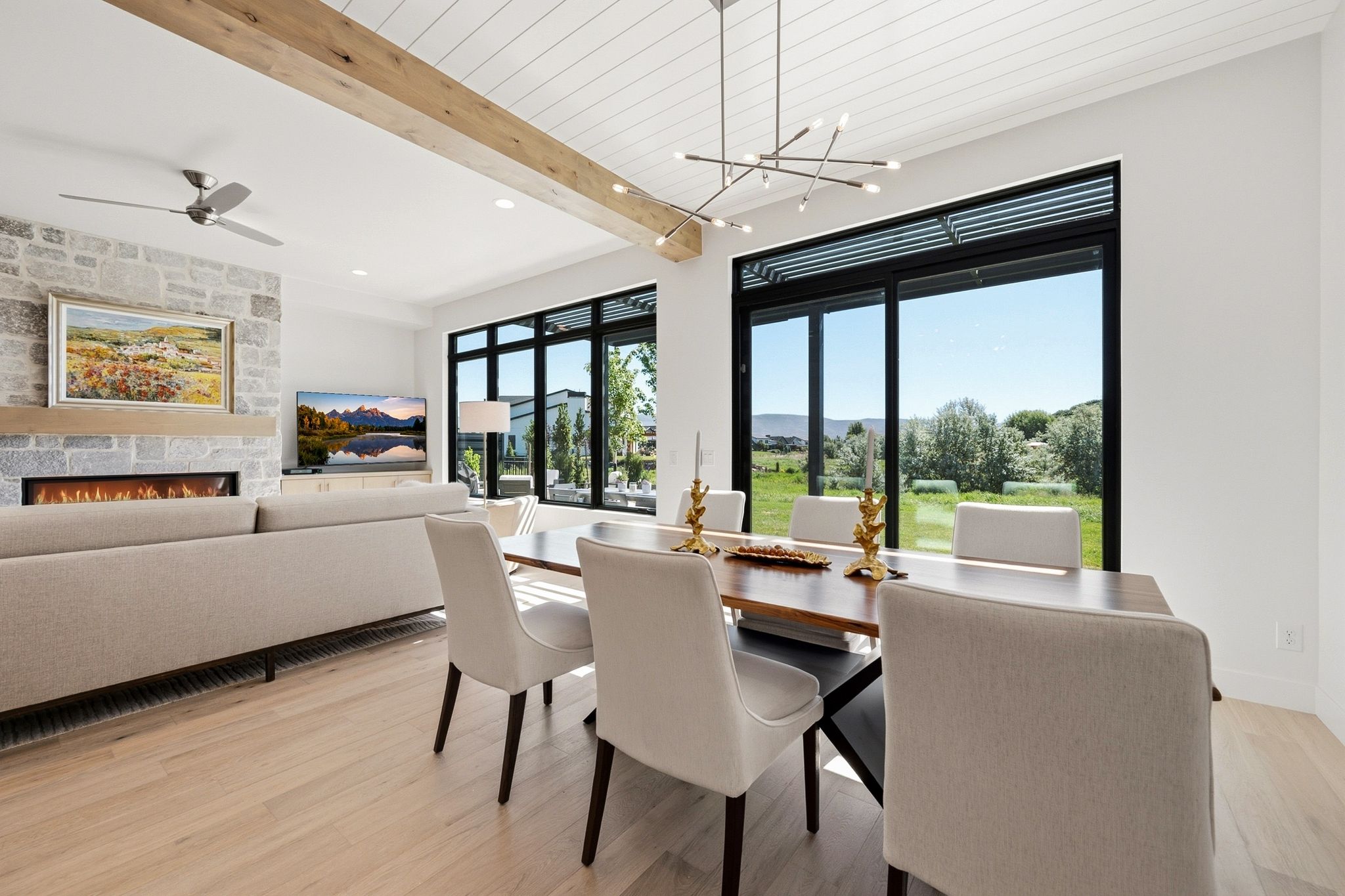 Open-concept living area featuring a stone fireplace with a wood mantle, a natural wood beam, and wood-finish flooring