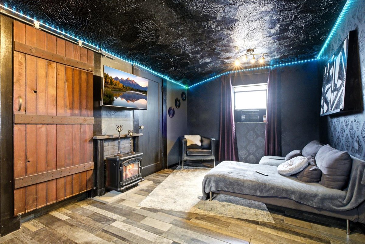 Room featuring wood-finish flooring, a wood-paneled sliding barn door, a built-in media center with a mounted television, a floor-standing fireplace, and a textured ceiling