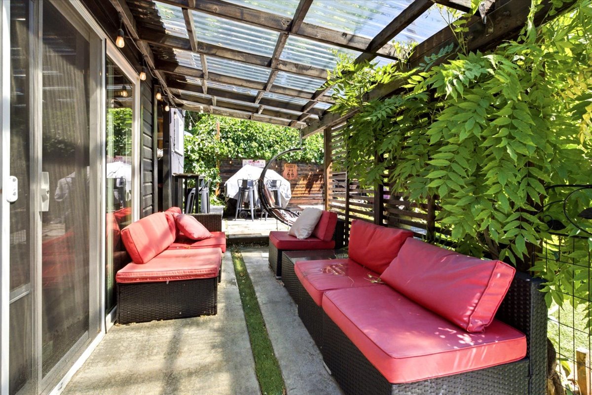 Covered patio featuring a translucent roof, slatted wood walls, and abundant foliage