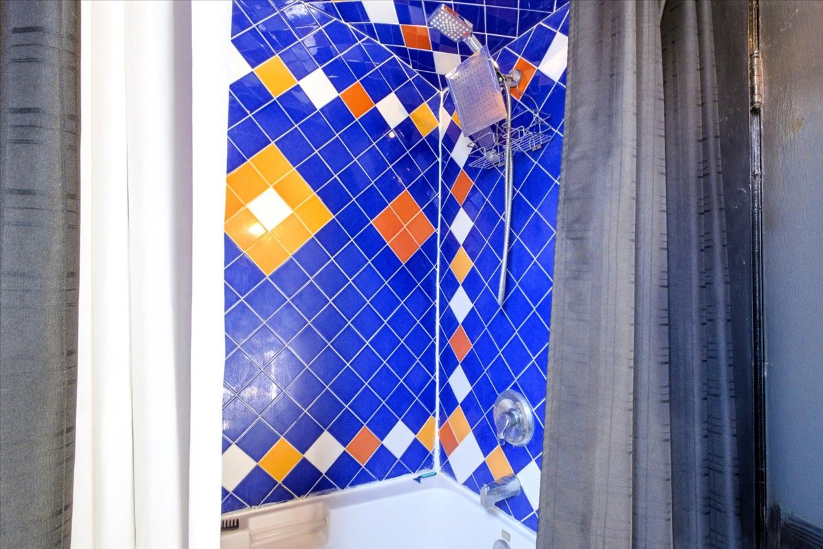 Bathtub with vibrant blue, orange, and white diamond-patterned wall tiling